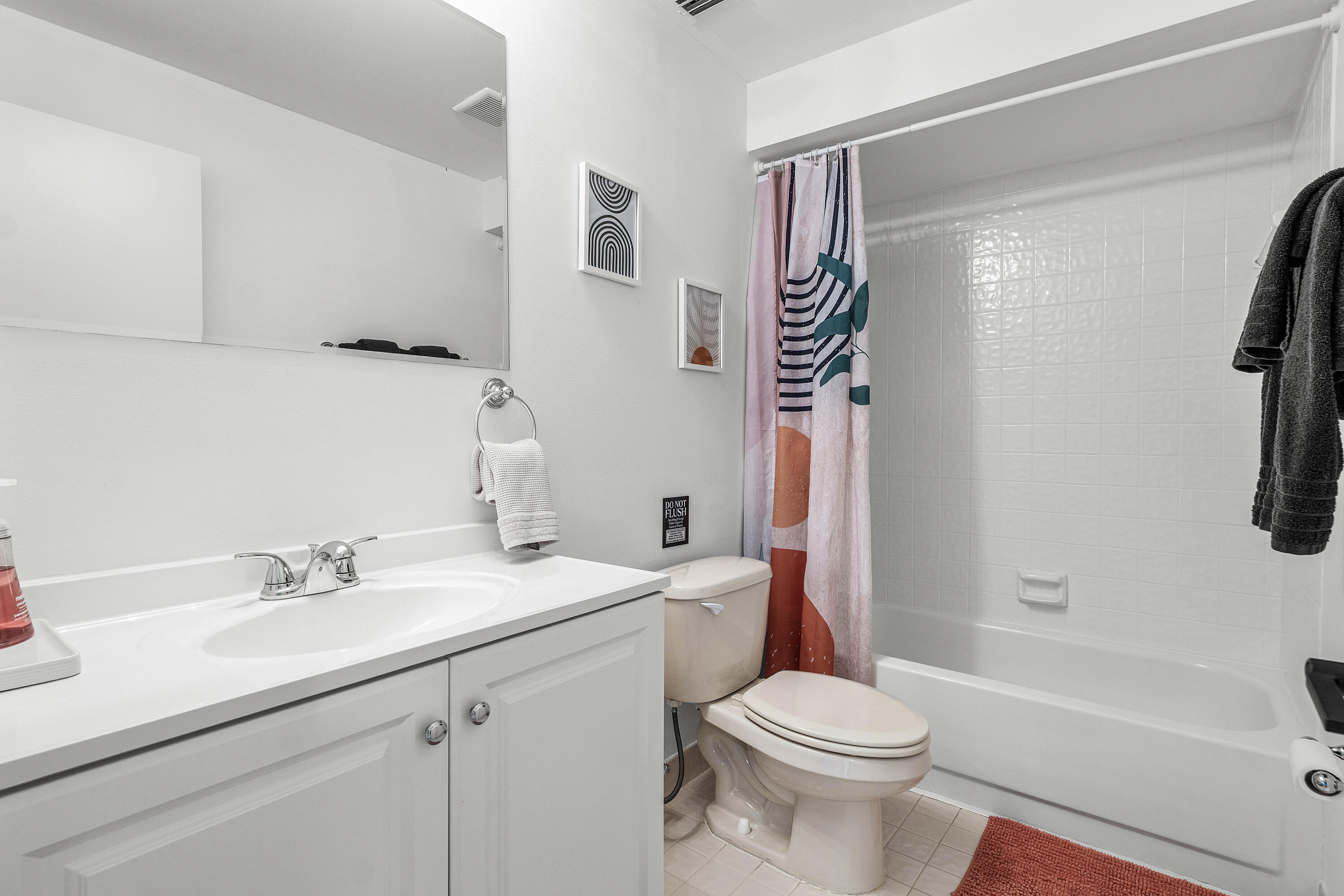 Bathroom featuring a white vanity cabinet, solid-surface countertop with an integrated basin, wall-mounted mirror, and a tub-shower combination with tile surround