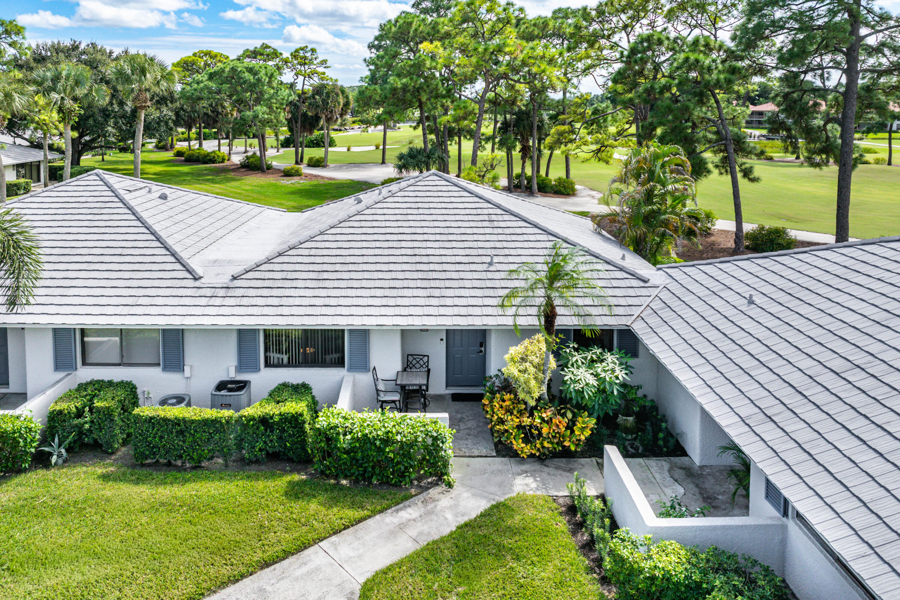 Exterior featuring a multi-gable tiled roof, light-toned stucco facade, decorative window shutters, and manicured landscaping