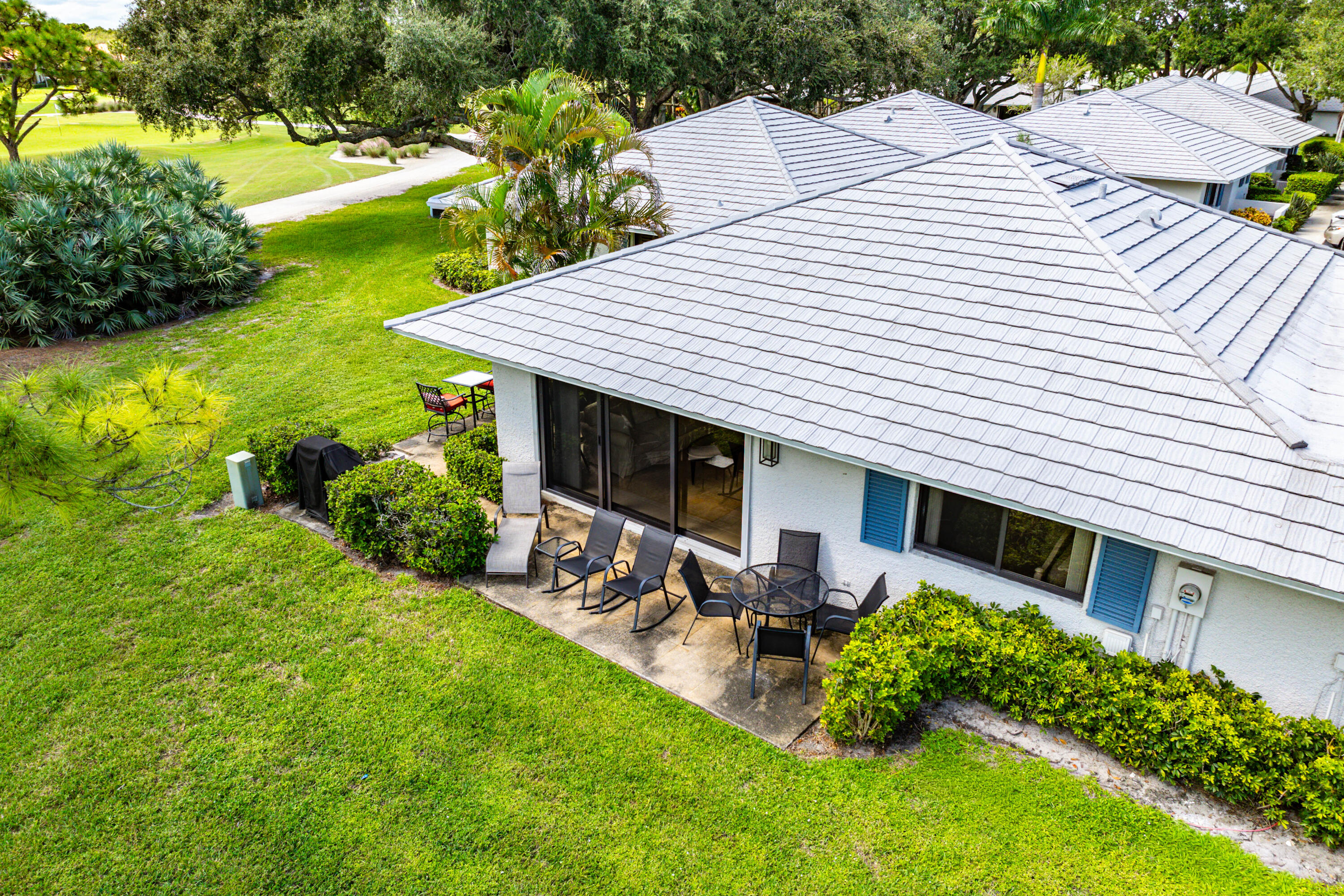 Exterior featuring a concrete tile roof, light-colored stucco siding, blue shutters, and a rear concrete patio