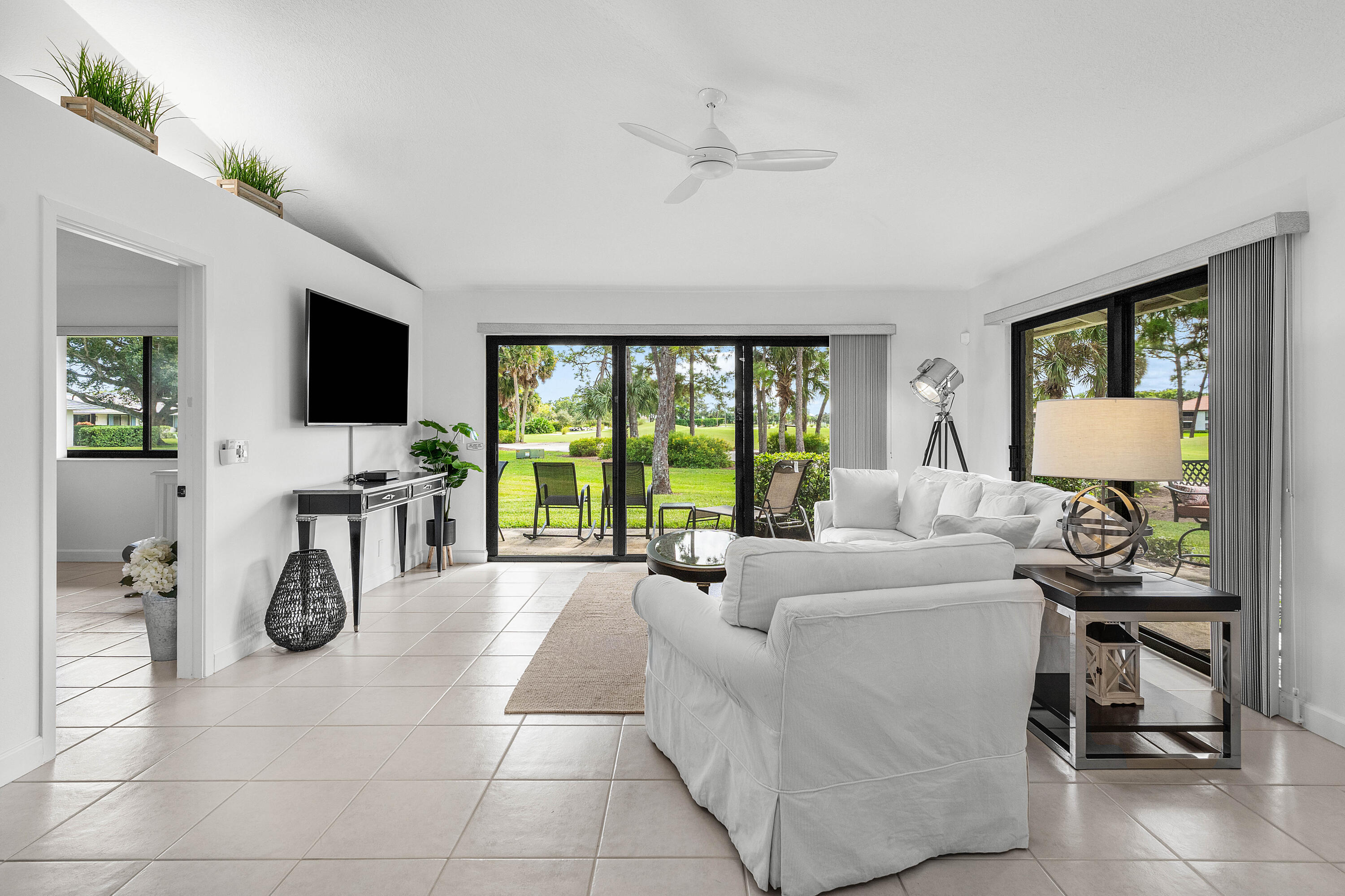 Living area featuring light-colored tile flooring, a vaulted ceiling with a white overhead fan, and two sets of sliding glass doors