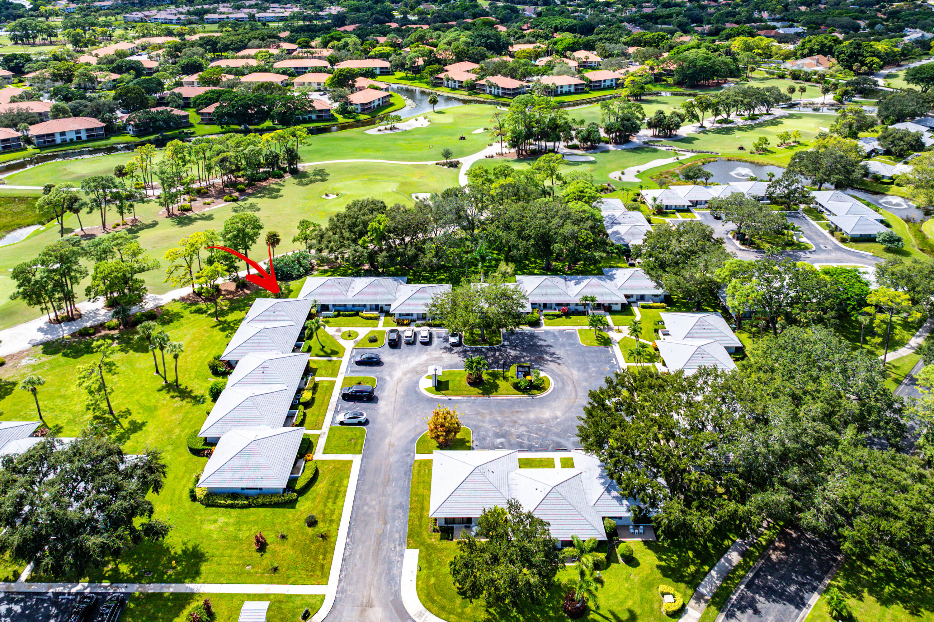 Aerial perspective of residential structures featuring multi-slope hip roofs, surrounding green space, paved parking areas, and mature landscaping