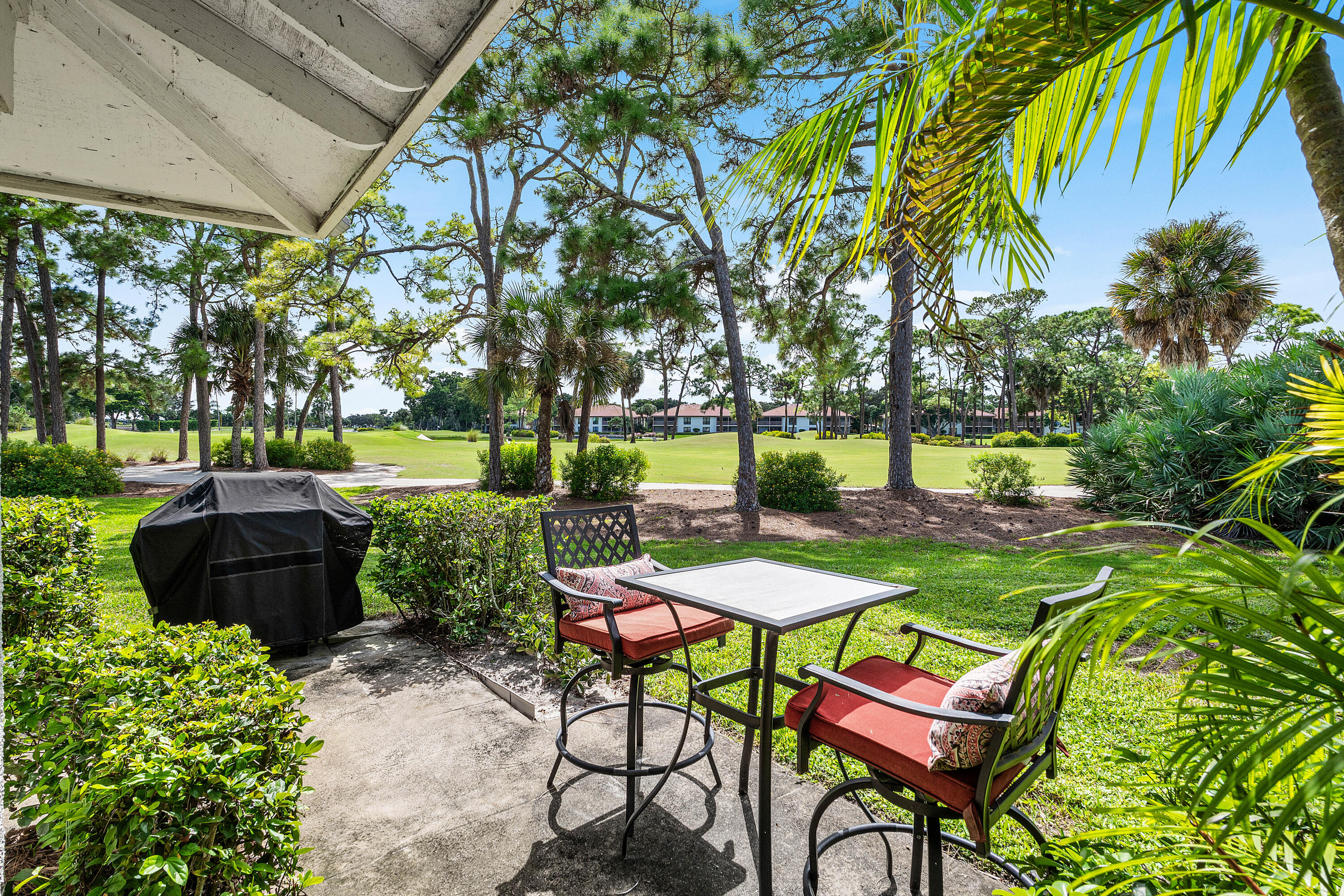 Covered concrete patio featuring landscape hedging and mature trees