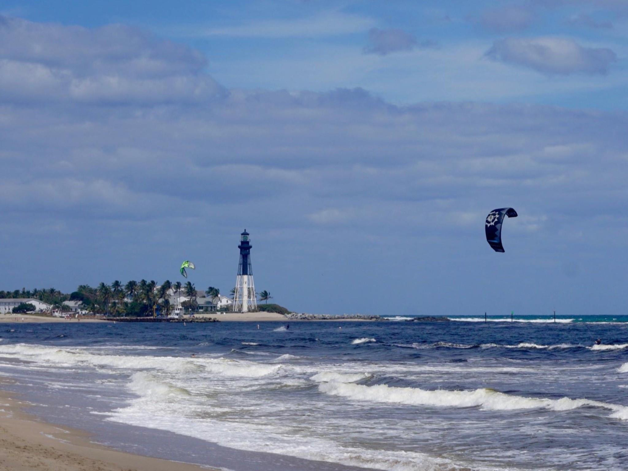 Sandy shoreline with ocean waves and a prominent lighthouse backdrop