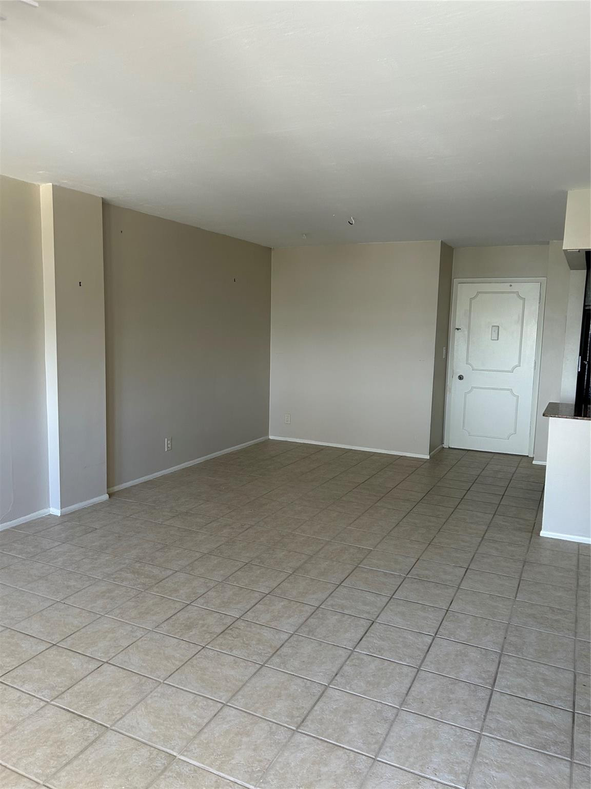 Open interior area featuring neutral wall paint, large-format ceramic tile flooring, and a paneled entry door