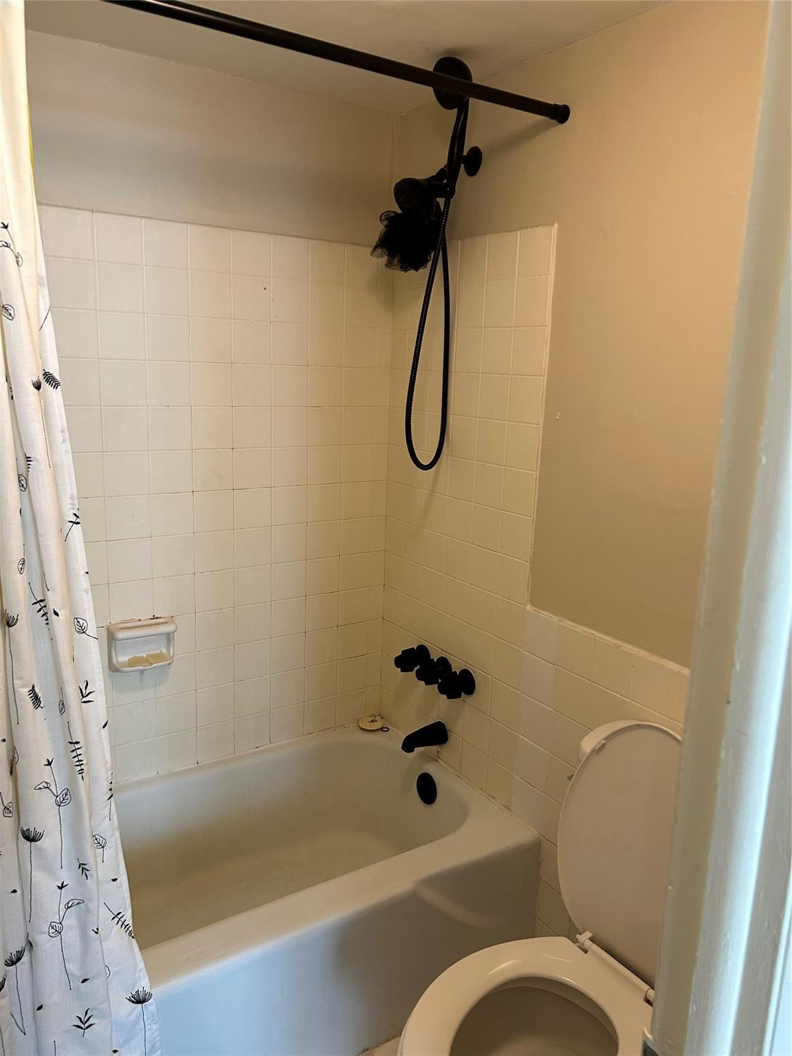 Bathtub and shower combination featuring square wall tiling, matte black fixtures, and an integrated soap dish