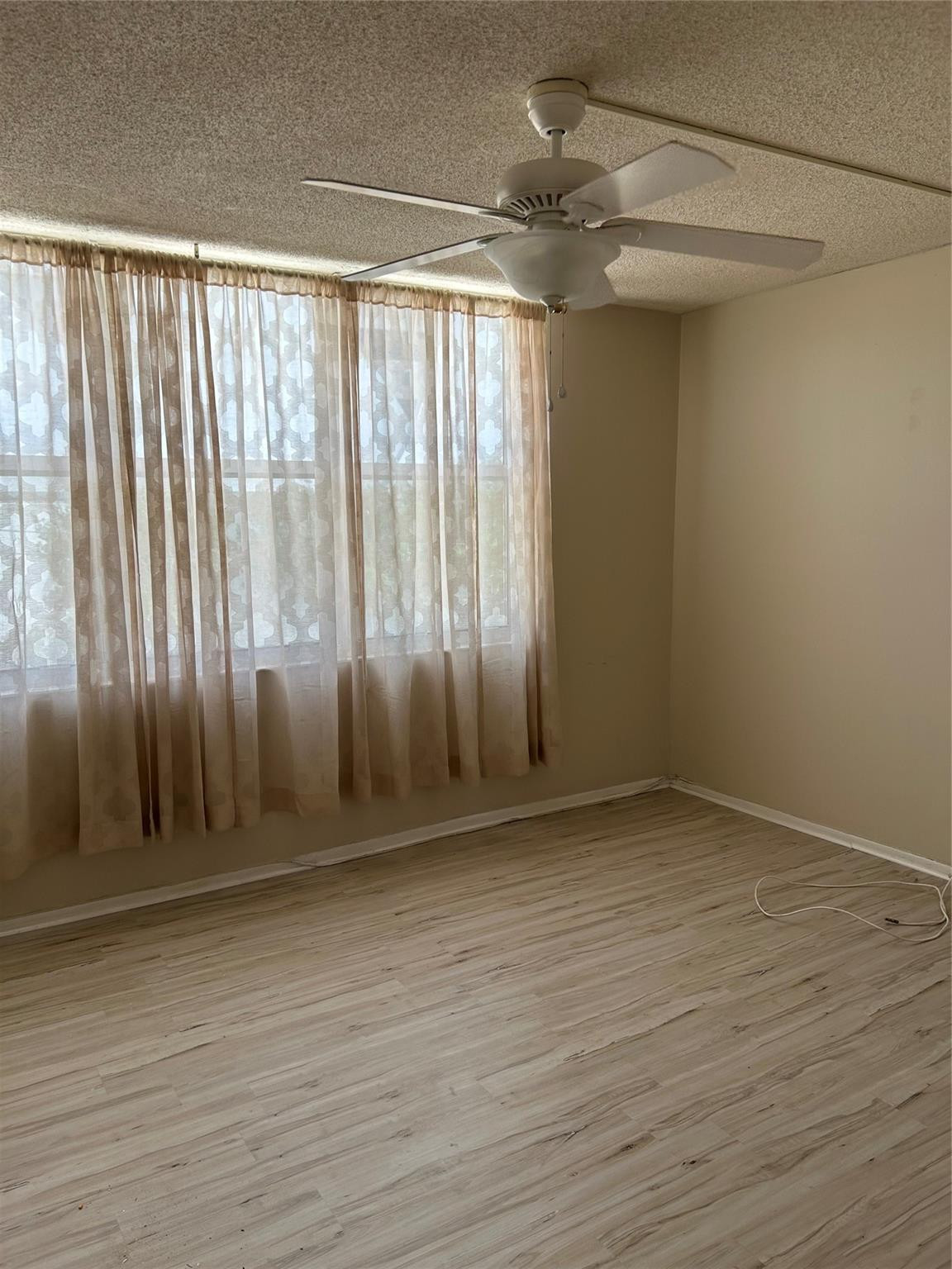 Room featuring wood-finish flooring, a white ceiling fan with an integrated light fixture, and floor-to-ceiling windows