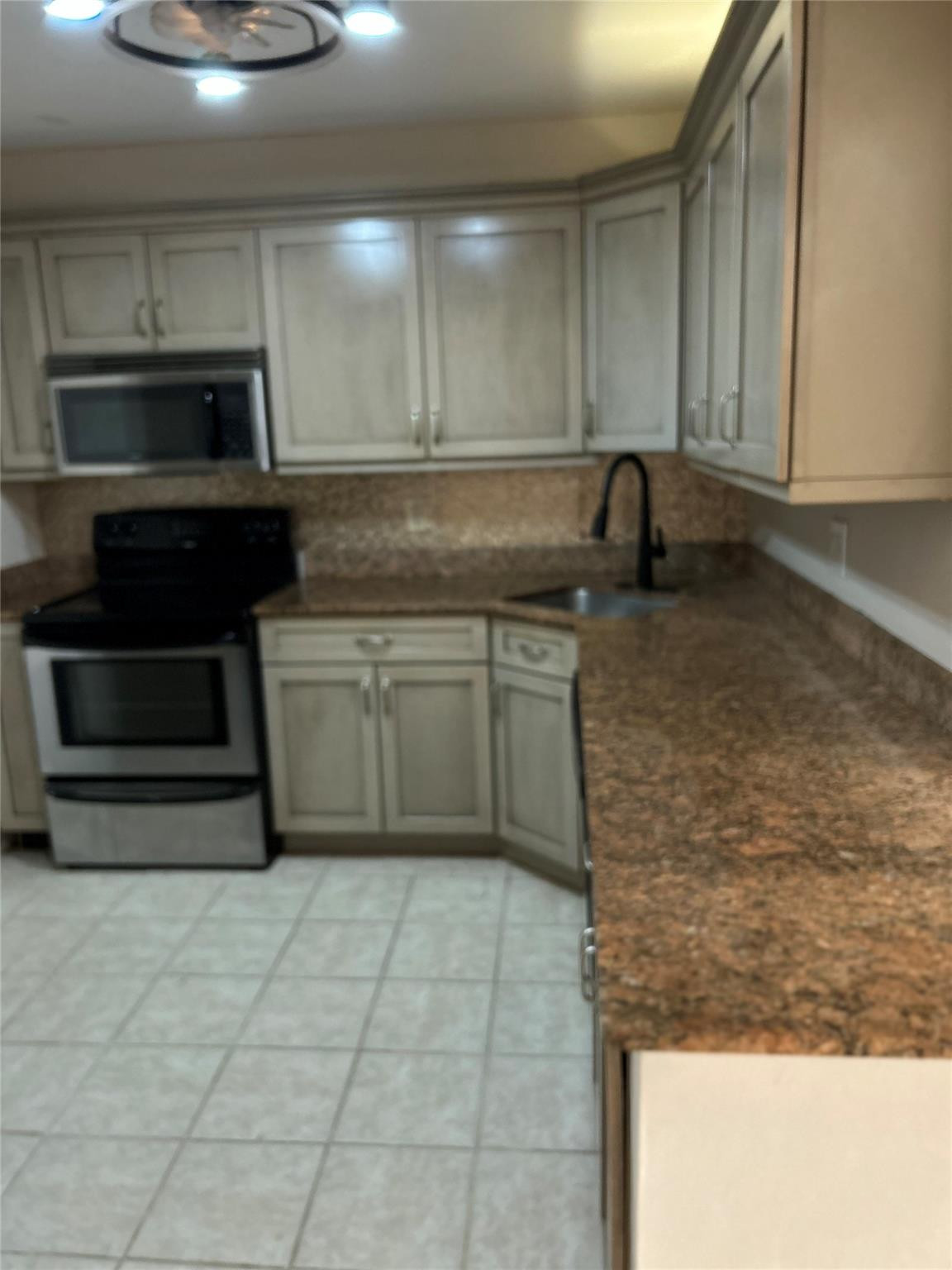 Kitchen featuring Shaker-style cabinetry, stone-finish countertops, stainless steel appliances, a high-arc faucet, and tiled flooring