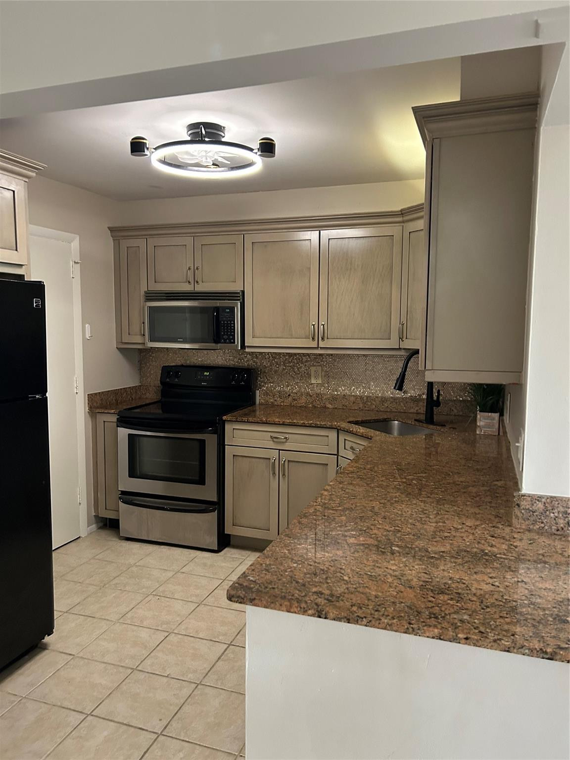 Kitchen featuring light-toned cabinetry, stone-finish countertops, stainless steel appliances, ceramic tile flooring, and a modern circular flush-mount ceiling fixture
