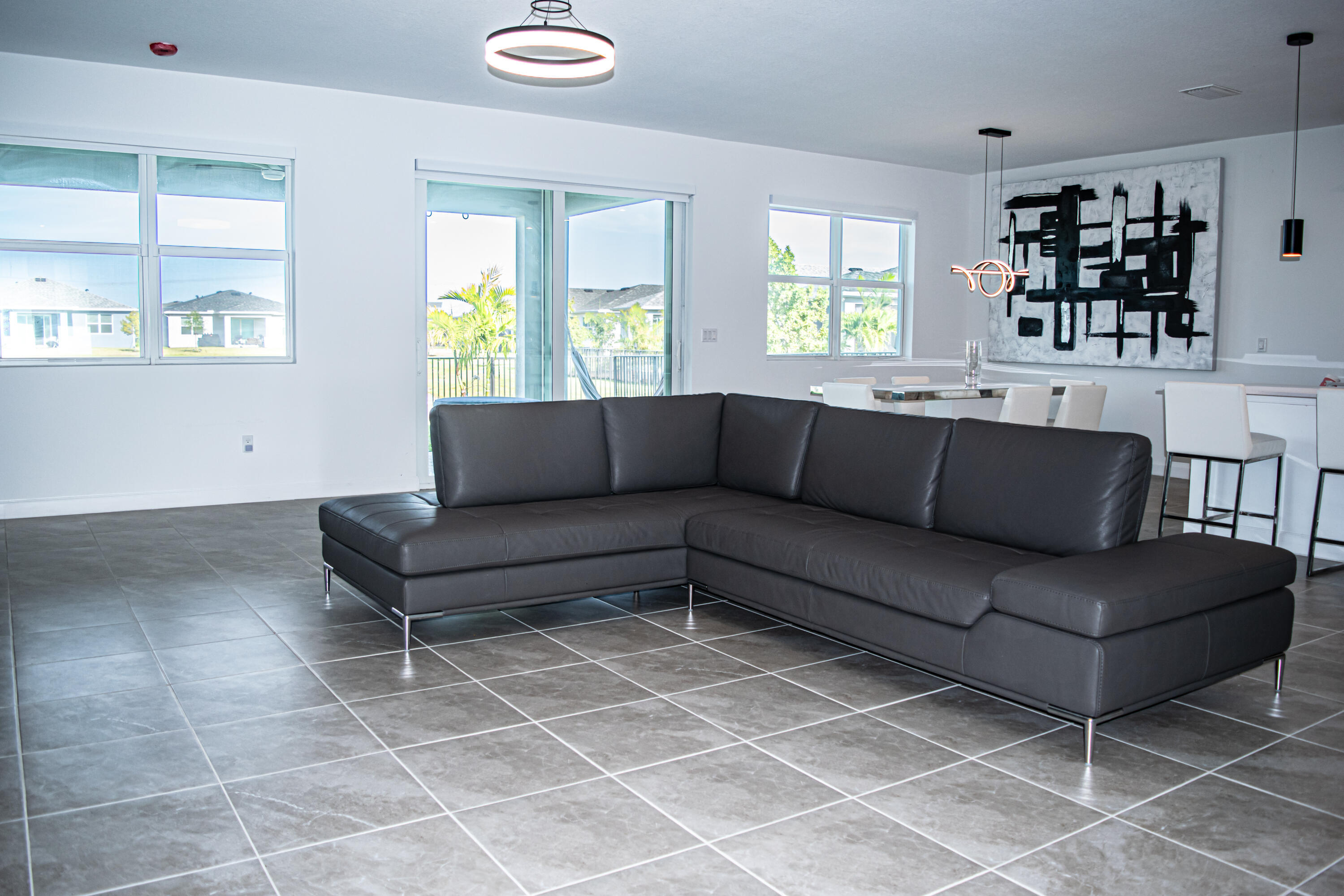 Open-concept interior featuring large-format ceramic tile flooring, multiple windows, sliding glass door, and modern multi-light fixtures
