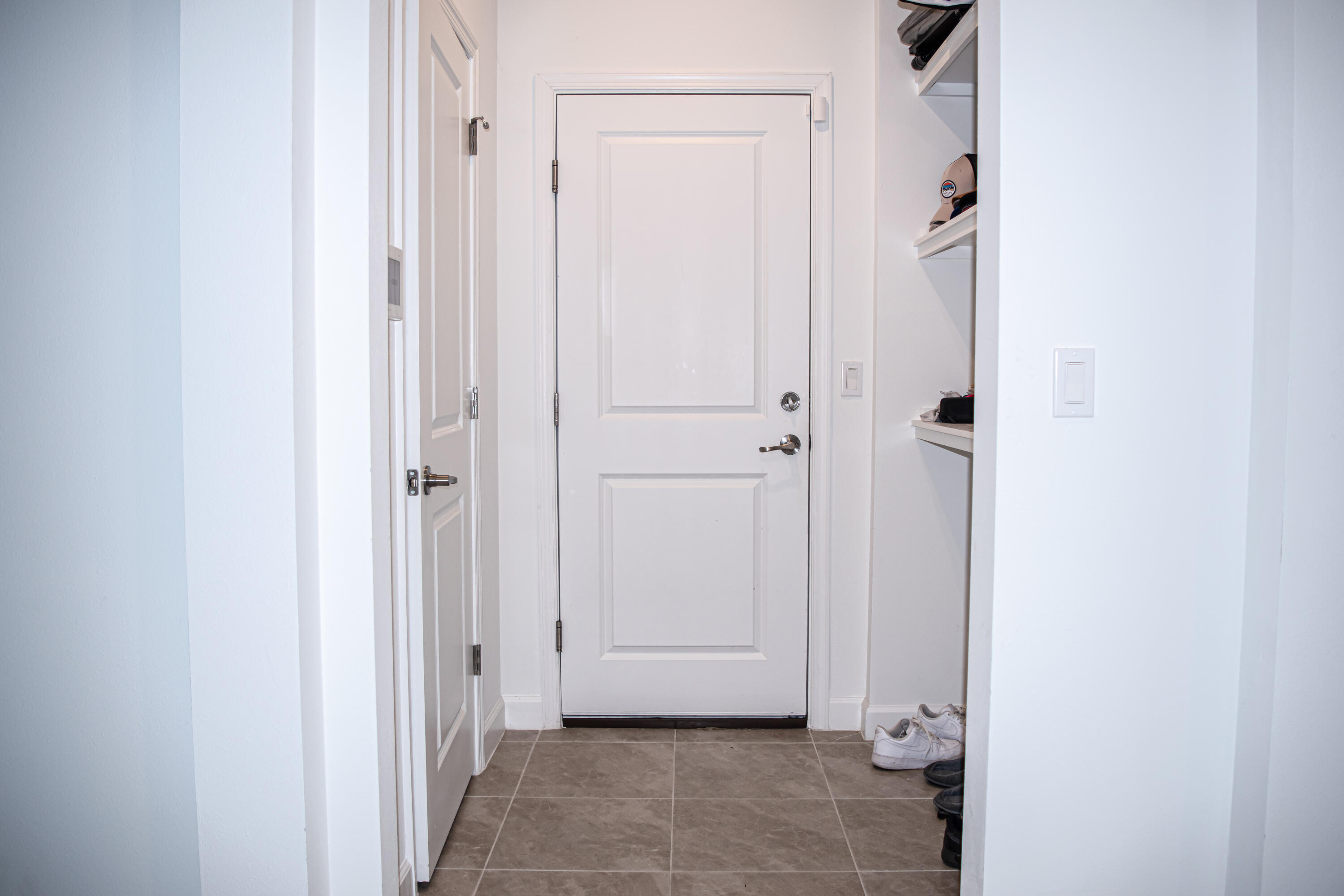 Neutral-toned stone-finish tile flooring featuring a white paneled door, integrated wall shelving, and a secondary interior door with metallic hardware