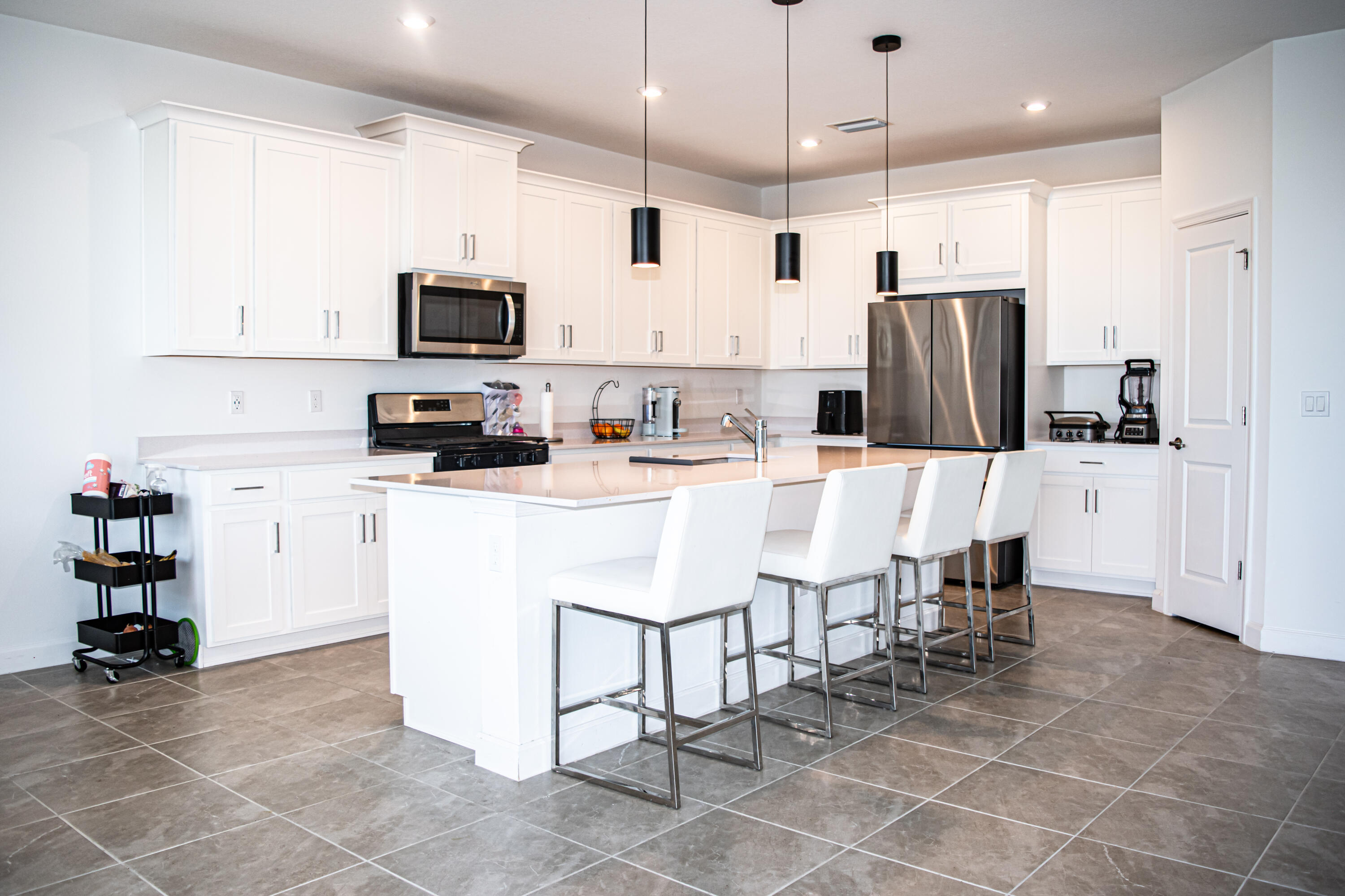 Kitchen featuring white shaker-style cabinetry, a central island with a stone-finish countertop, stainless steel appliances, pendant lighting, and tile flooring