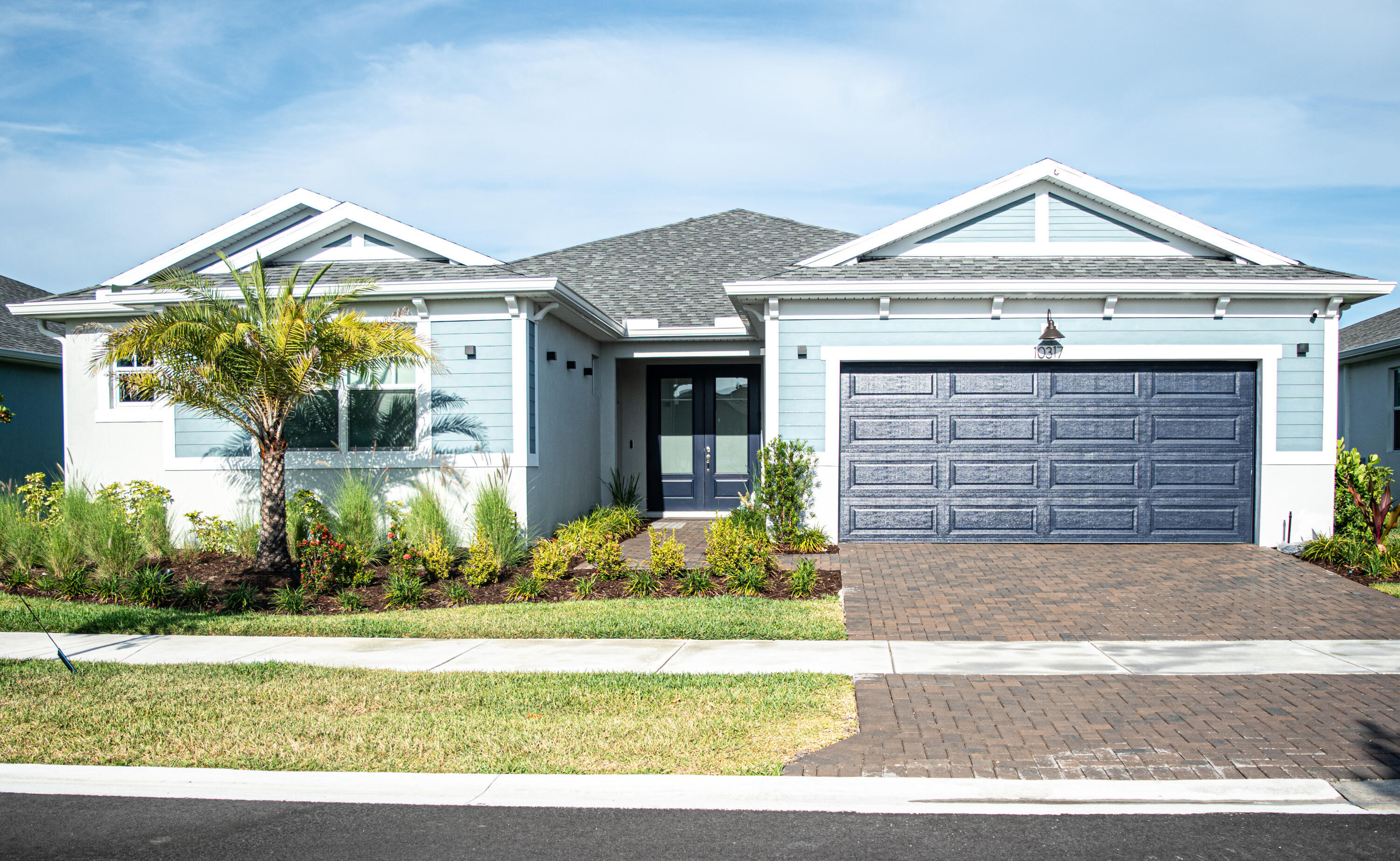 Single-story exterior featuring blue horizontal lap siding, a two-car paneled garage door, a paver driveway, double front entry doors, and gable rooflines Single-story exterior featuring blue horizontal lap siding, a two-car paneled garage door, a paver driveway, double front entry doors, and gable rooflines
