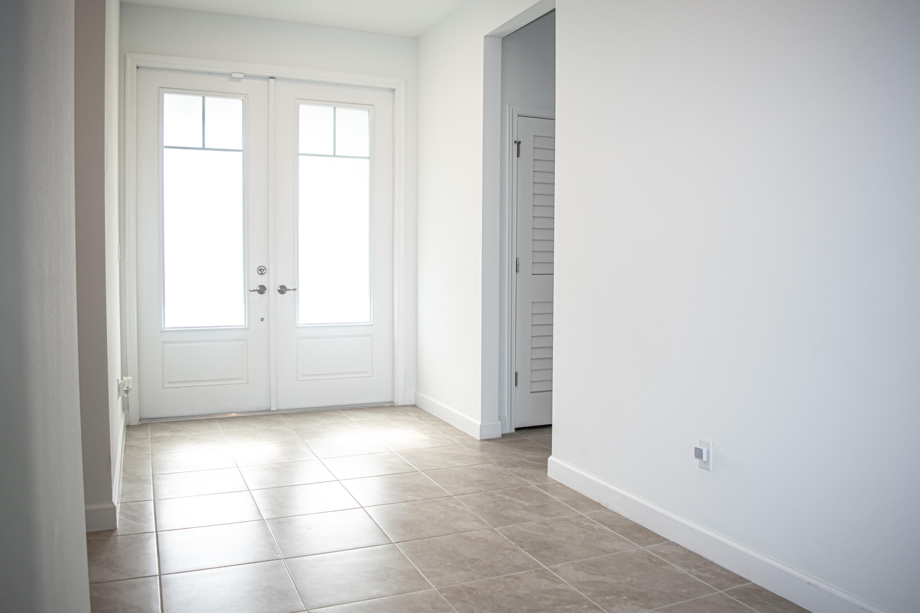 Entryway featuring double glass-paneled doors, neutral tile flooring, and white interior doors with louvered accents