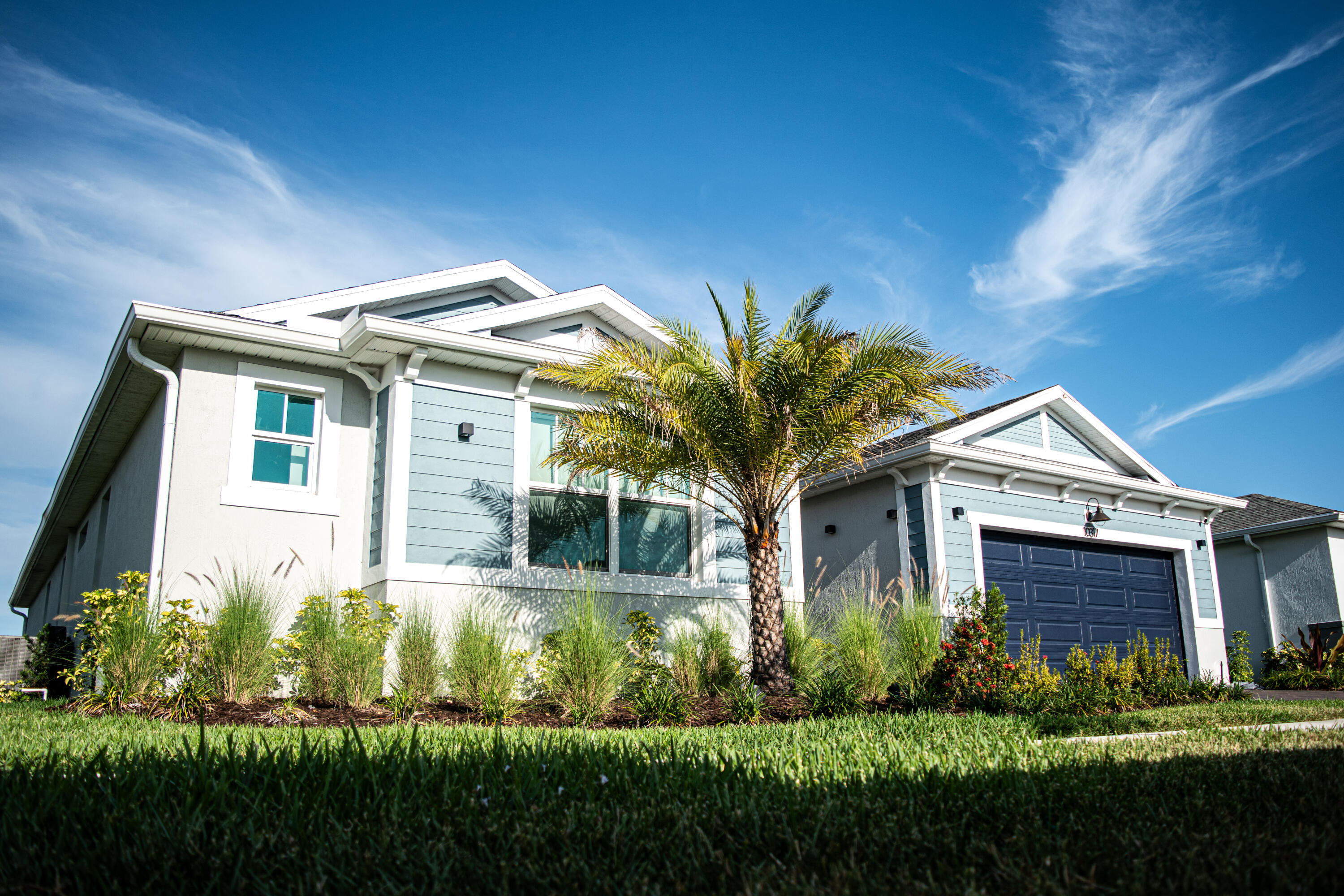 Exterior featuring horizontal lap siding, a gabled roofline, an attached two-car garage, and landscaped garden beds with established ornamental grasses