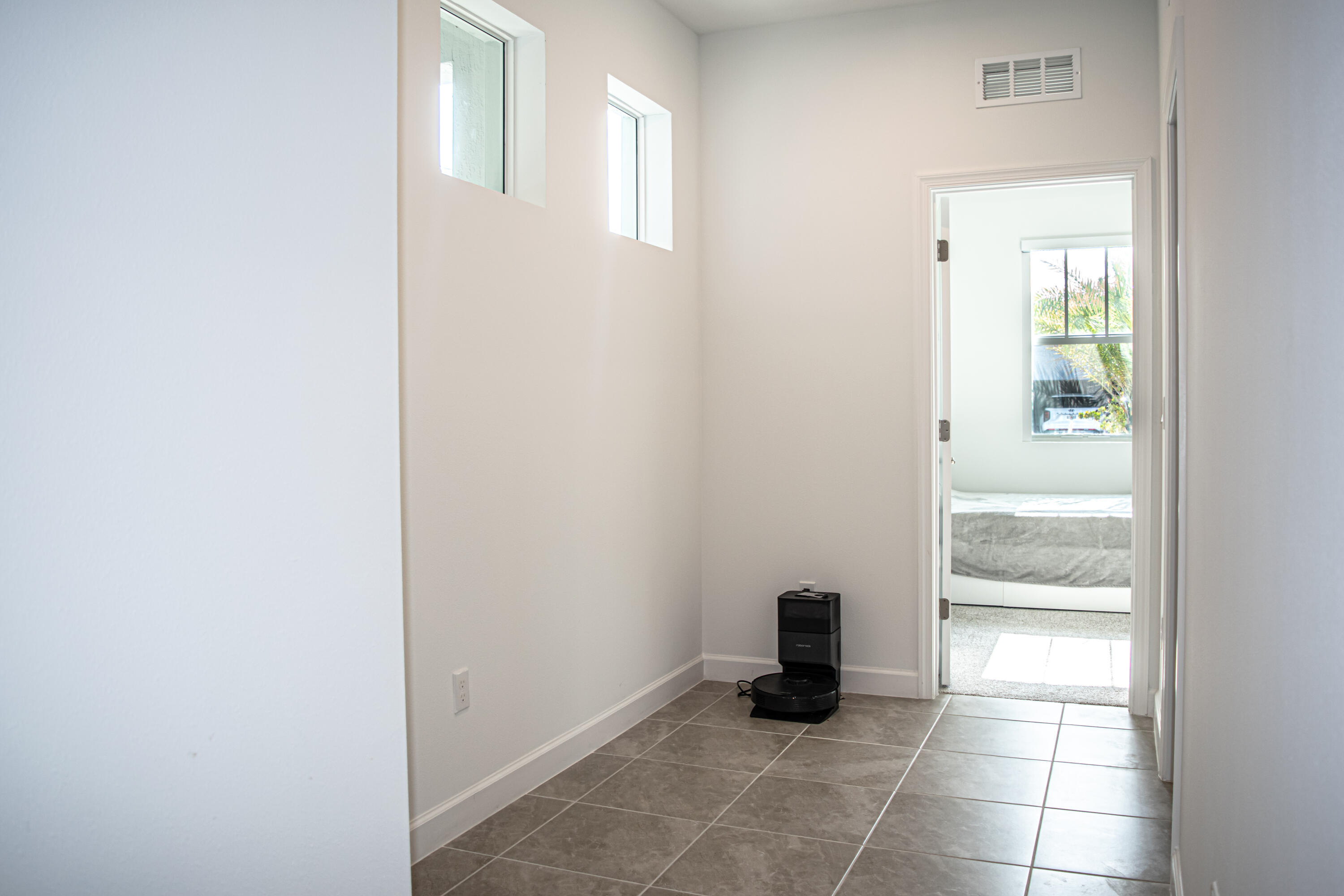 Neutral-toned tile flooring, two square clerestory windows, and a doorway opening into a secondary room featuring a large window