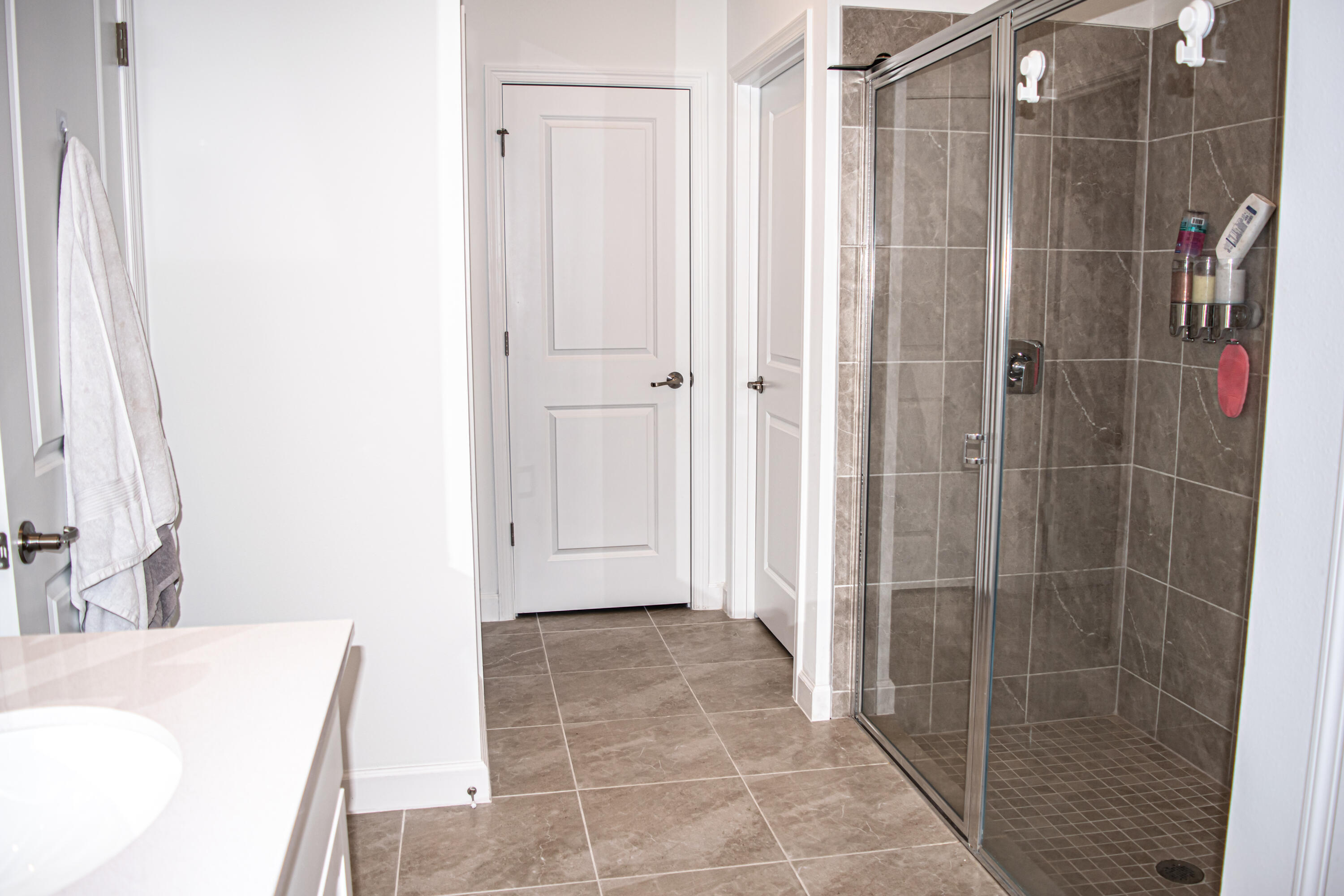 Bathroom featuring a walk-in shower with glass enclosure, neutral tile flooring, tiled shower walls, and a vanity with a solid-surface countertop