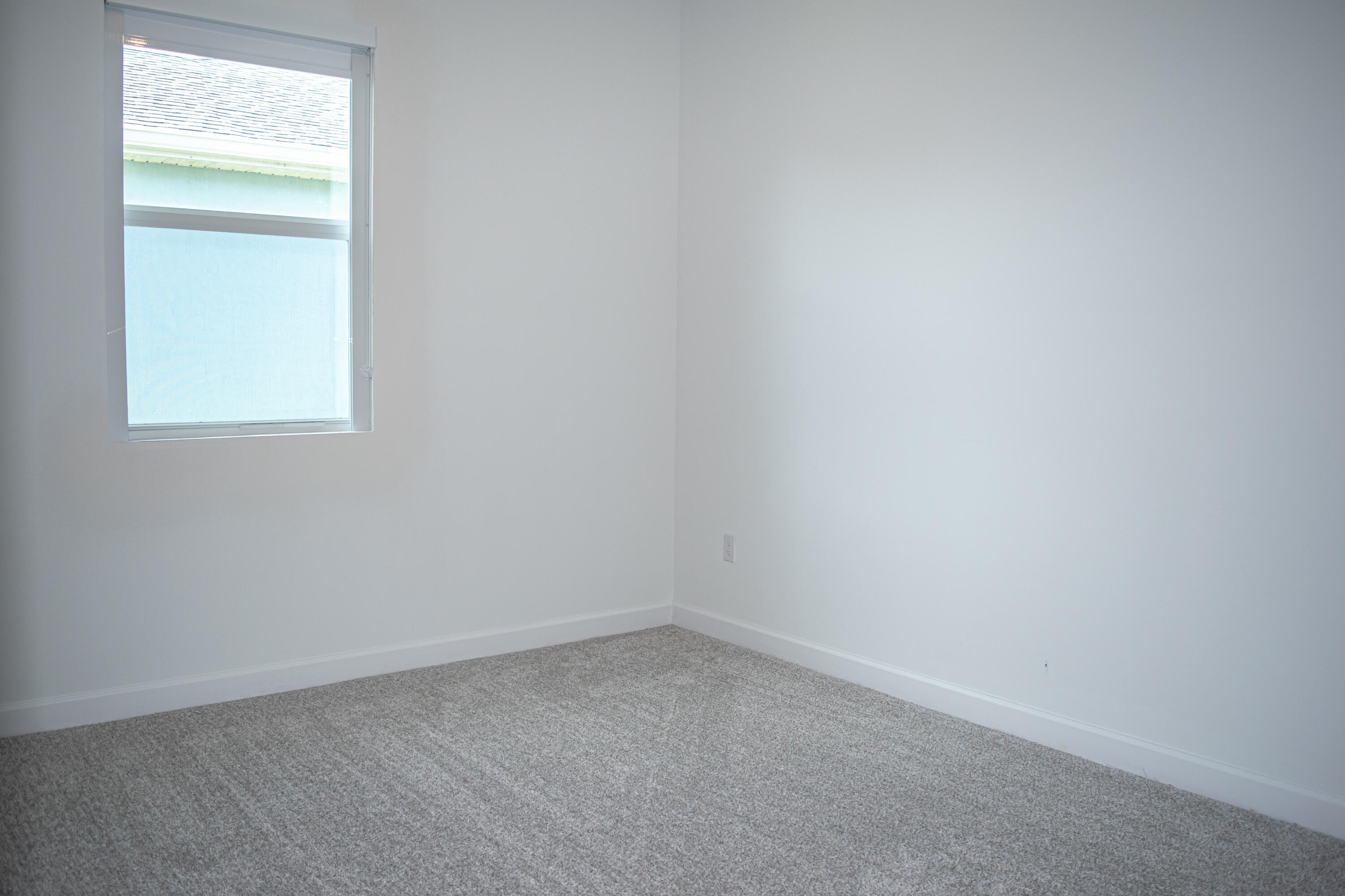 Neutral interior room featuring neutral-toned carpeting and a window with a fitted roller shade