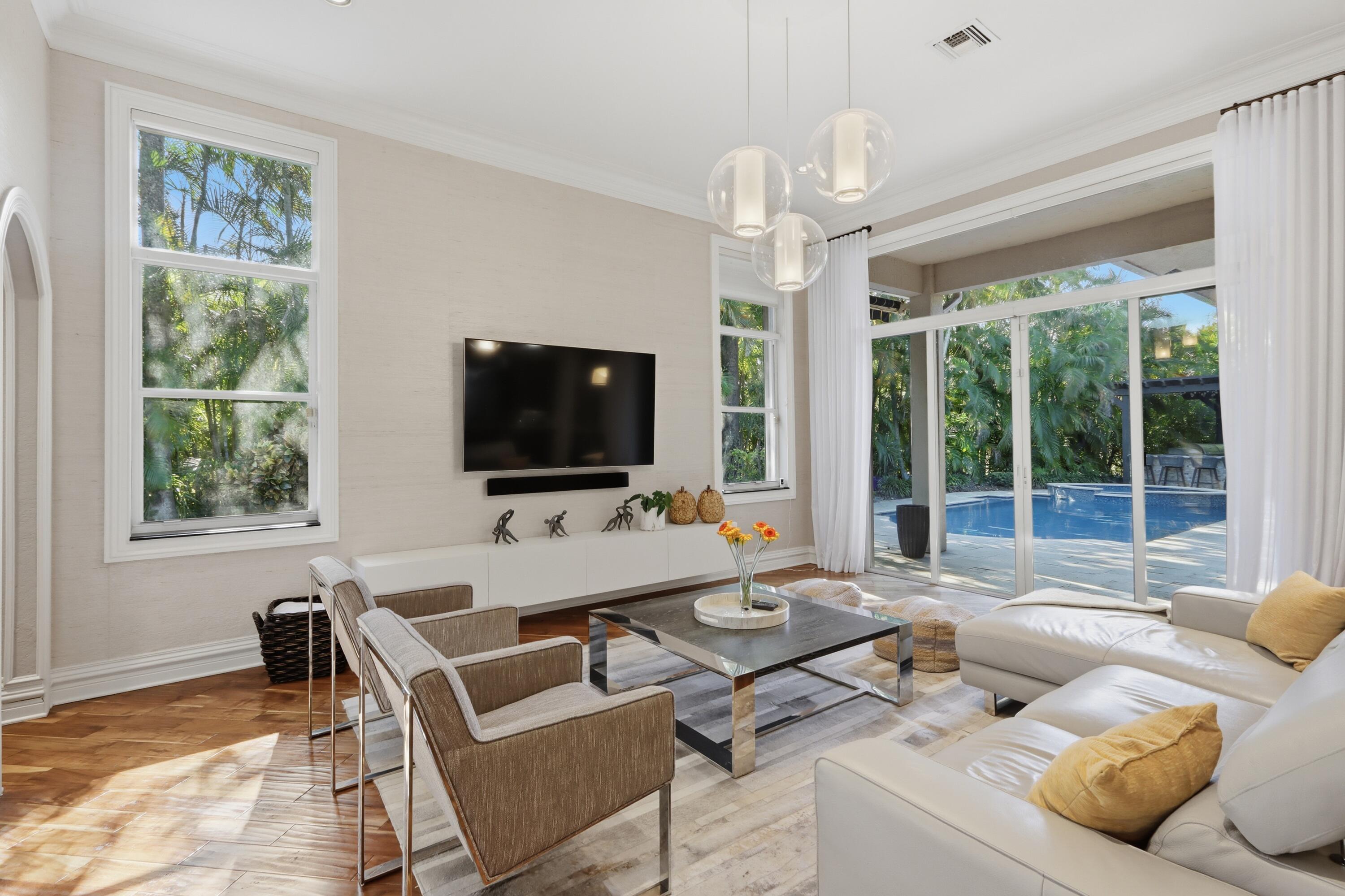 Living area featuring wood-finish flooring, multi-light glass pendant fixture, crown molding, and large-format glass sliding doors opening to an outdoor pool area