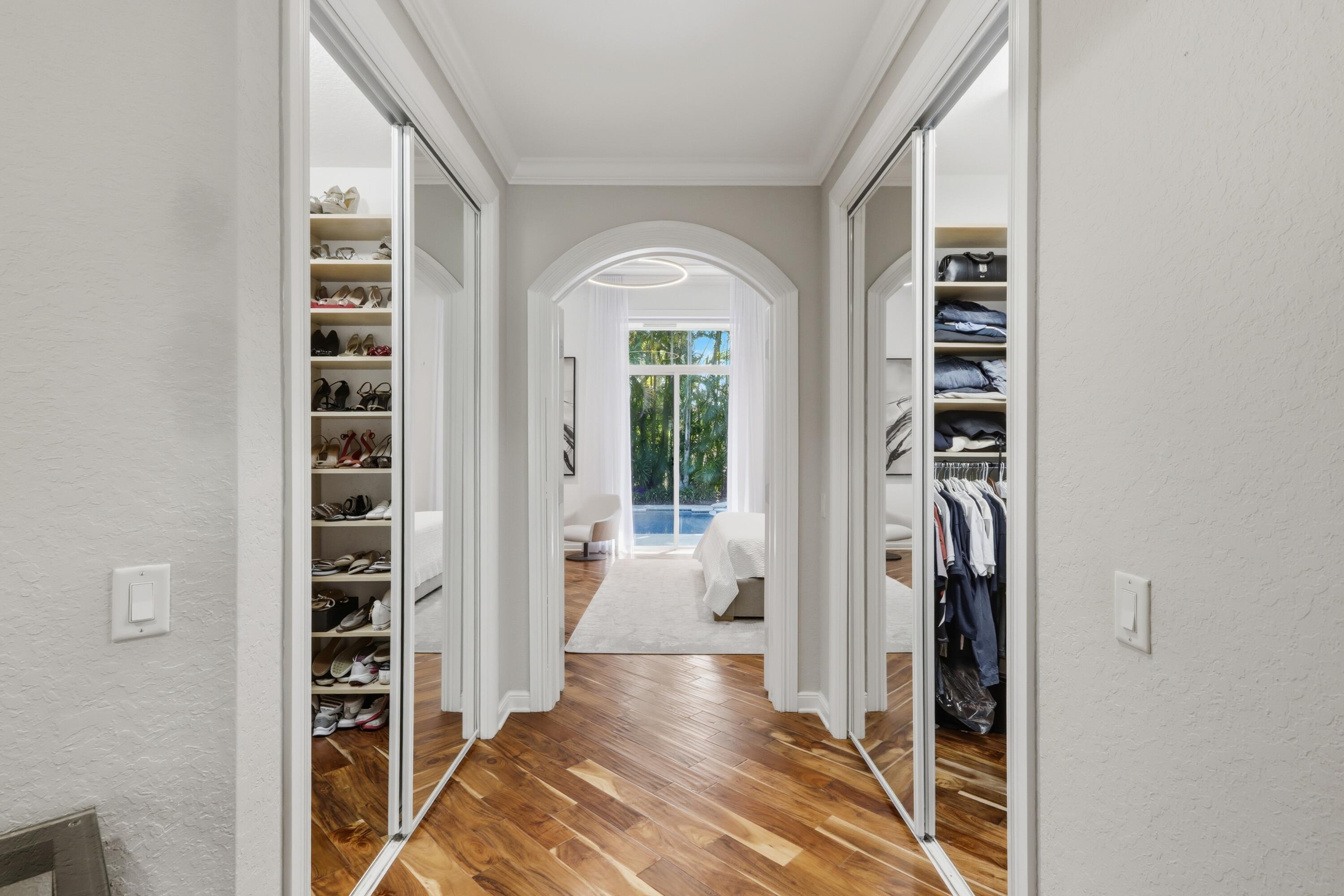 His and Hers walk-in wardrobe featuring mirrored sliding doors, custom integrated shelving, wood-finish flooring, and a decorative arched entryway