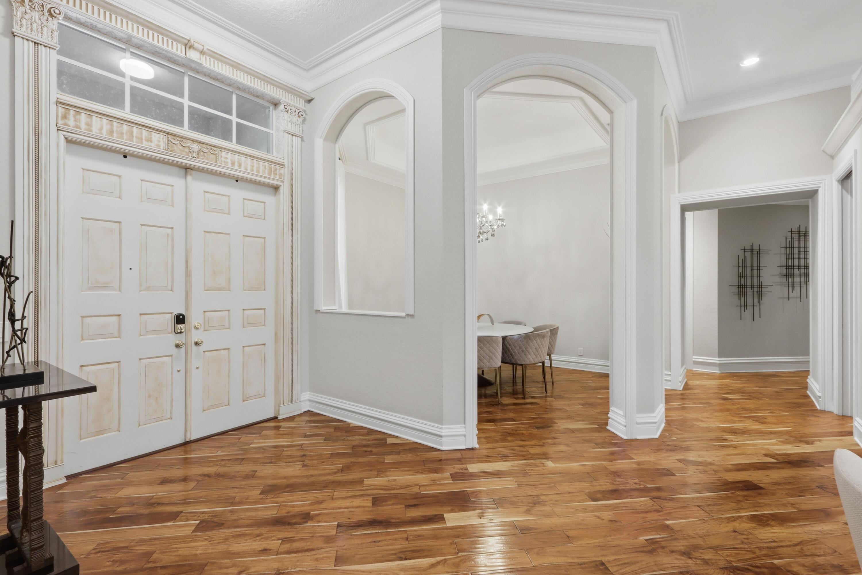 Foyer featuring wood-finish flooring, double entry doors with transom window, arched architectural openings, and extensive crown molding