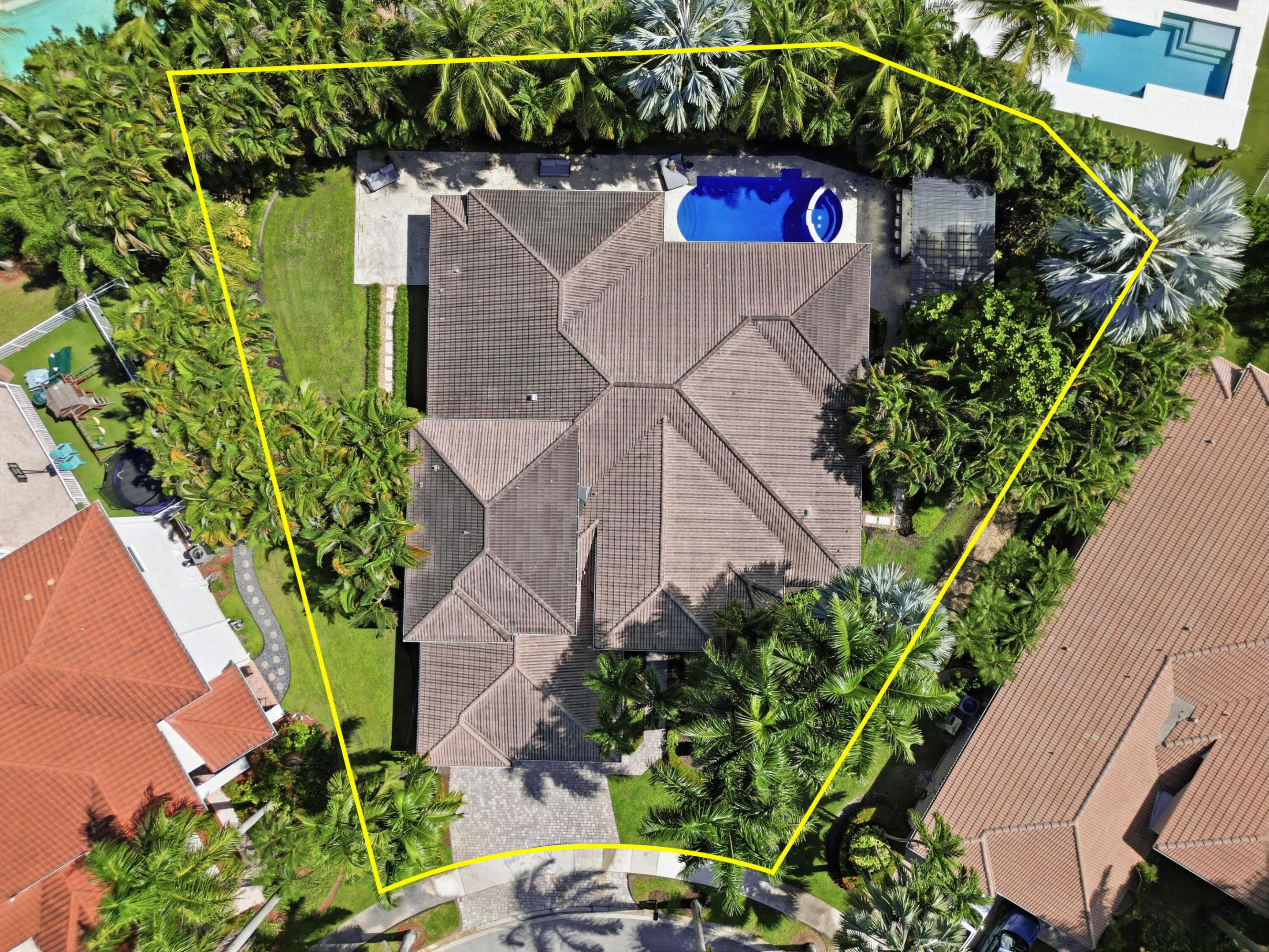 Aerial view of property featuring a hip roof, swimming pool with integrated spa, stone-paver driveway, and manicured landscaping