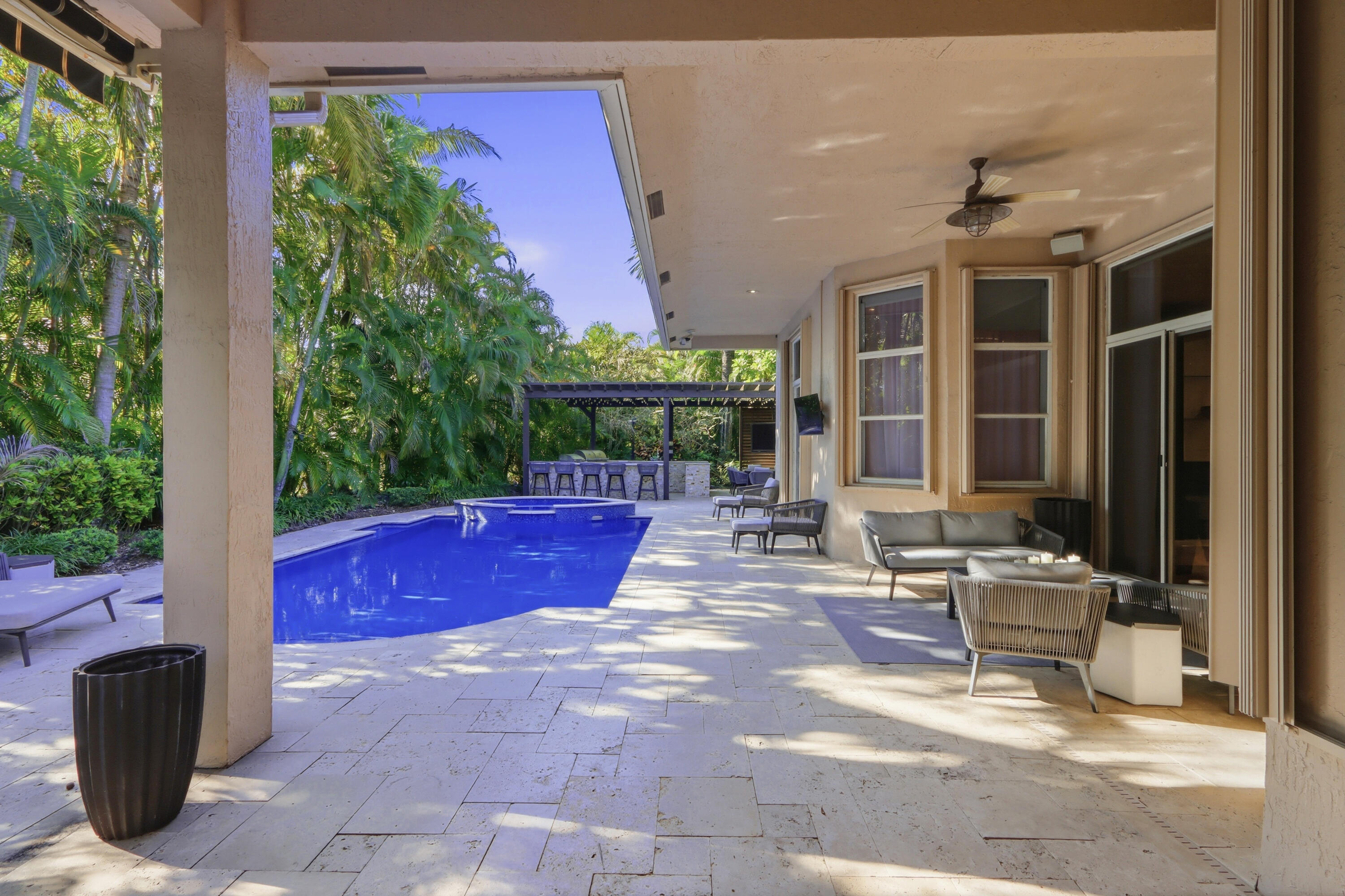 Covered patio featuring stone-tile flooring, a swimming pool with integrated spa, and an outdoor kitchen structure with a pergola