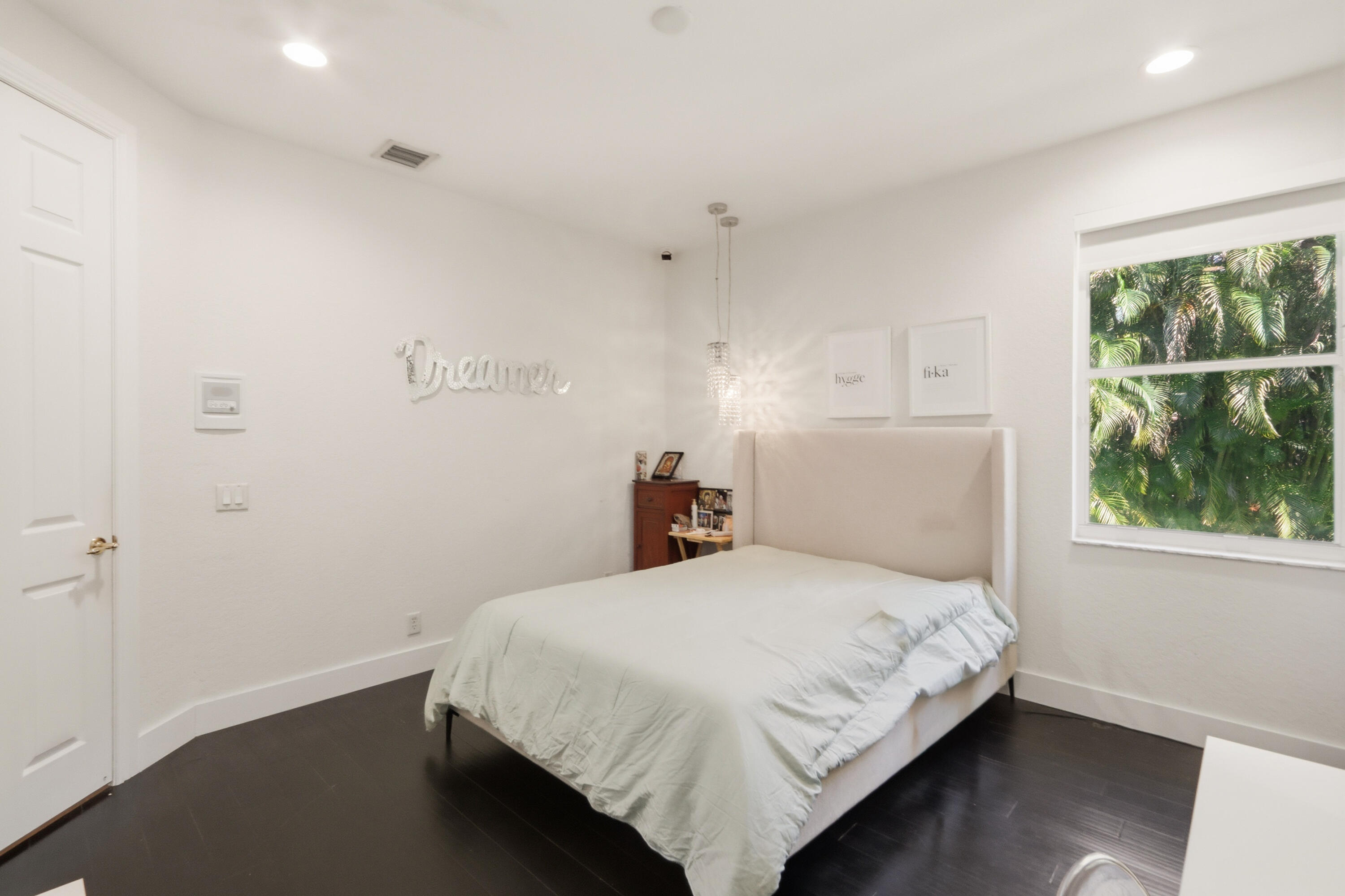 Bedroom featuring dark wood-finish flooring, recessed lighting, a multi-bulb hanging pendant light, and a window with natural scenery