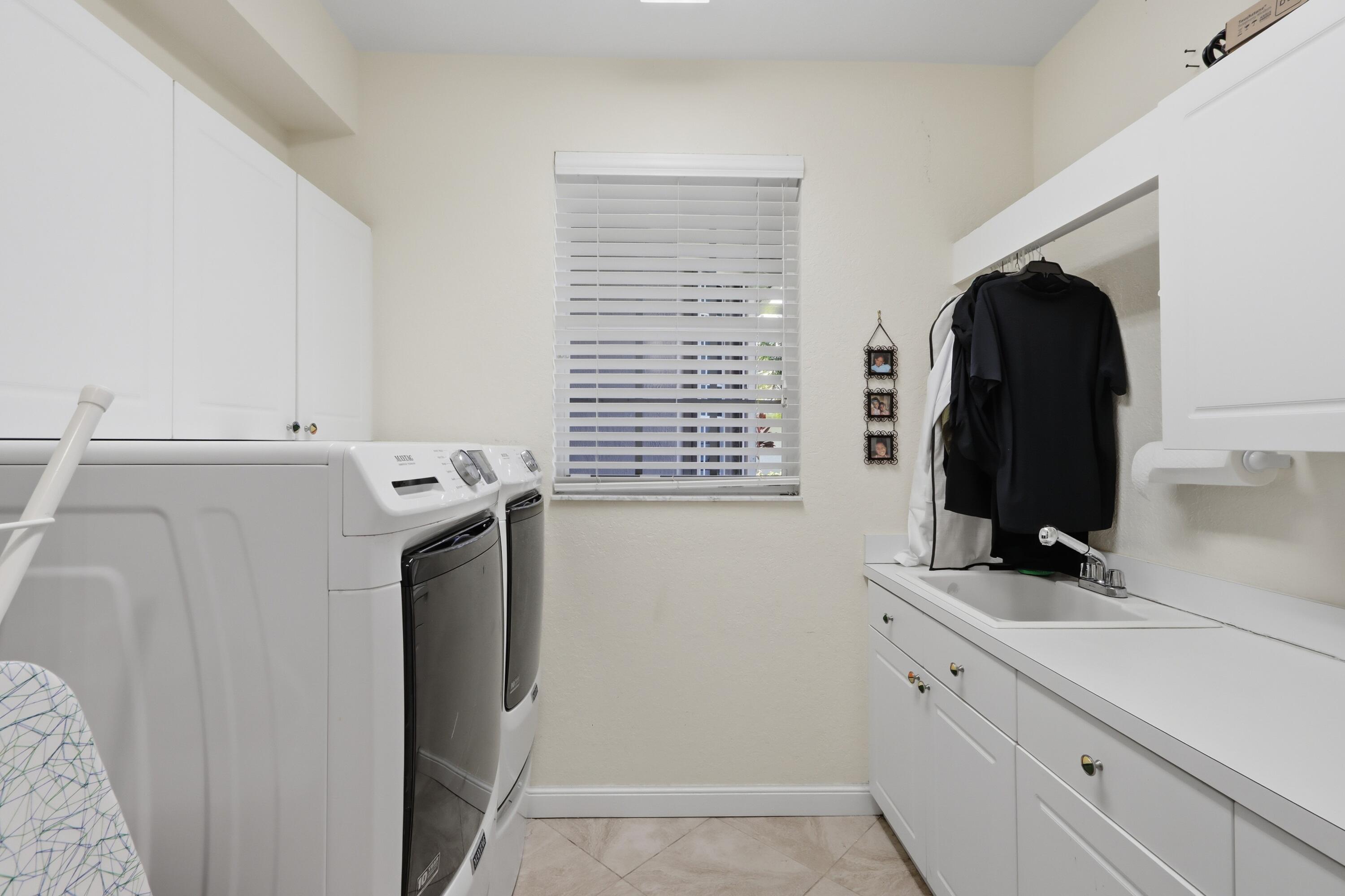 Laundry area featuring white shaker-style cabinetry, a drop-in utility sink with a chrome faucet, solid-surface countertops, and a window with horizontal blinds