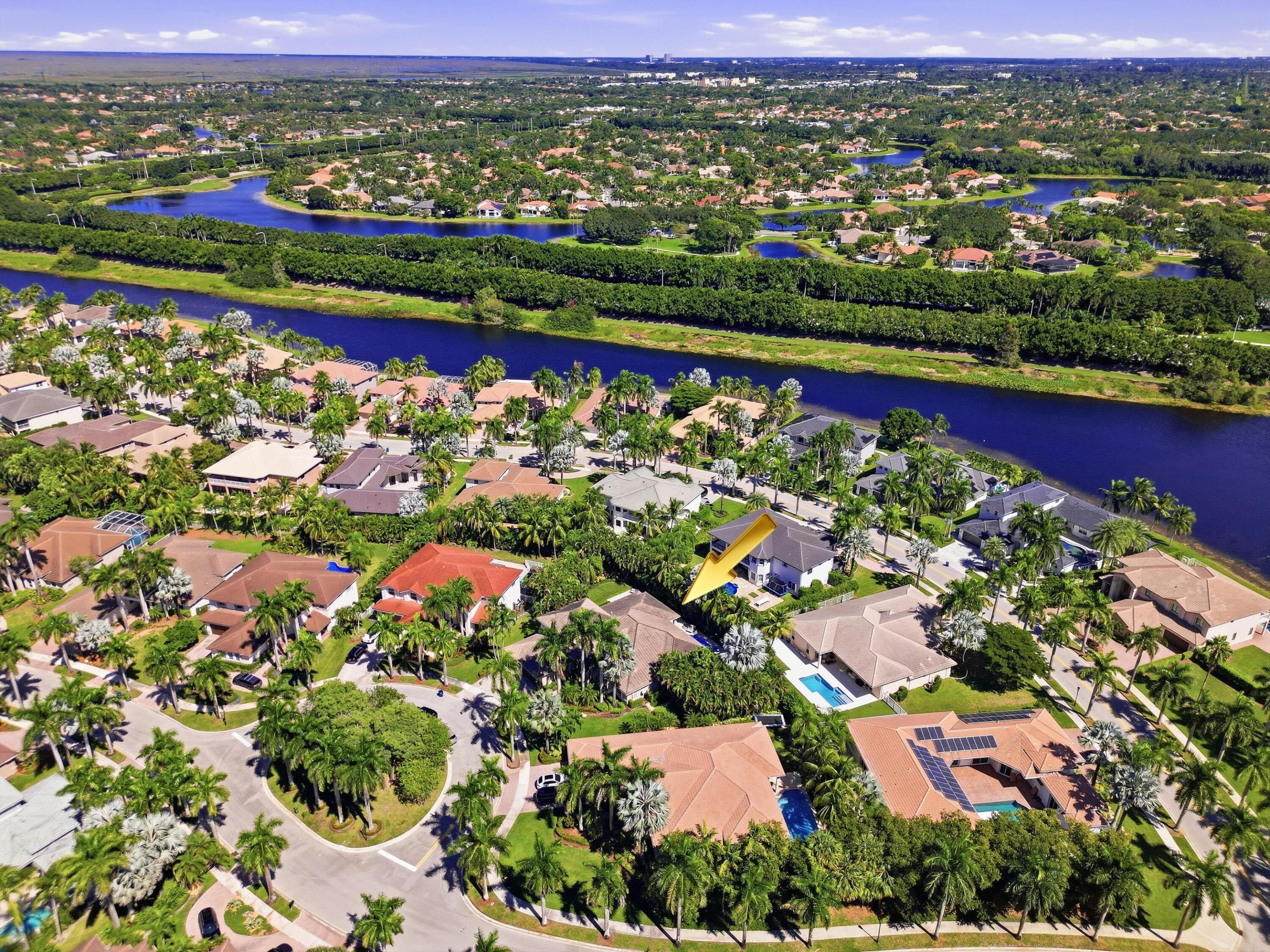 Aerial perspective of a residential property situated in a suburban community featuring canal-side positioning, mature palm trees, and terracotta-style roof tiles