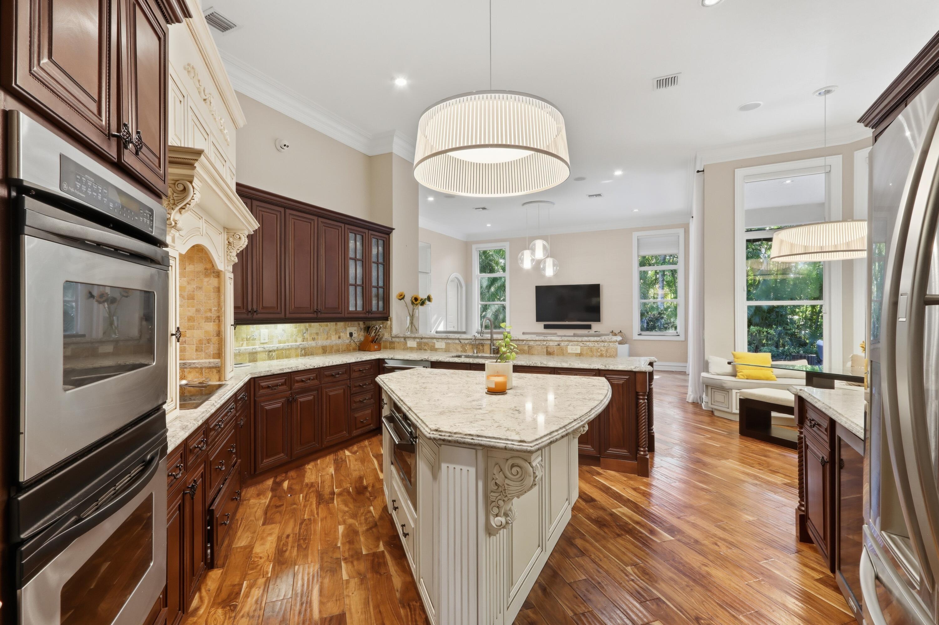Kitchen featuring wood-finish flooring, stone countertops, custom cabinetry, stainless steel double wall ovens, and an expansive center island