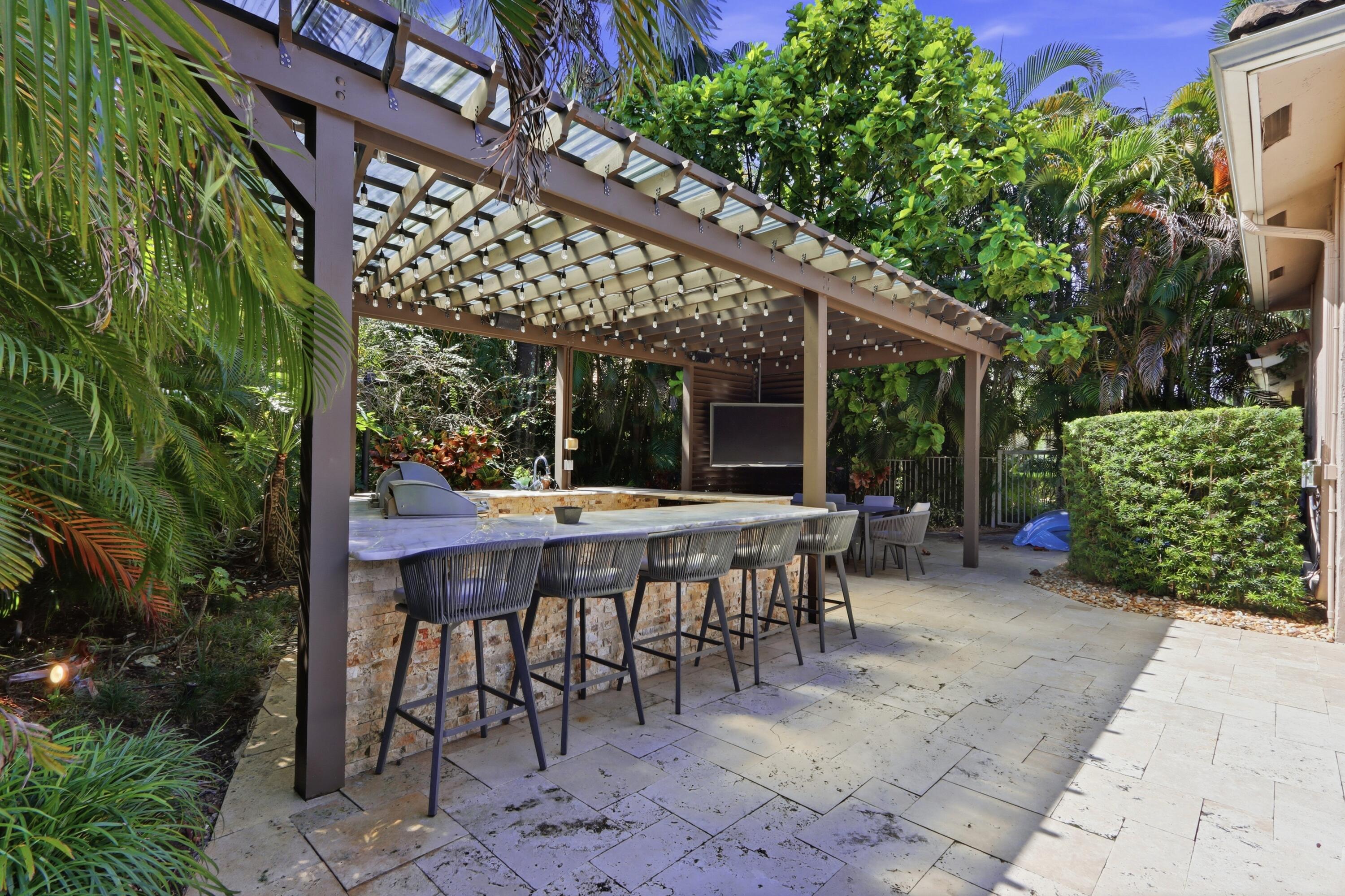 Outdoor kitchen area featuring a stone-clad bar, integrated grill, stone-tile patio, and a pergola with a slatted roof structure