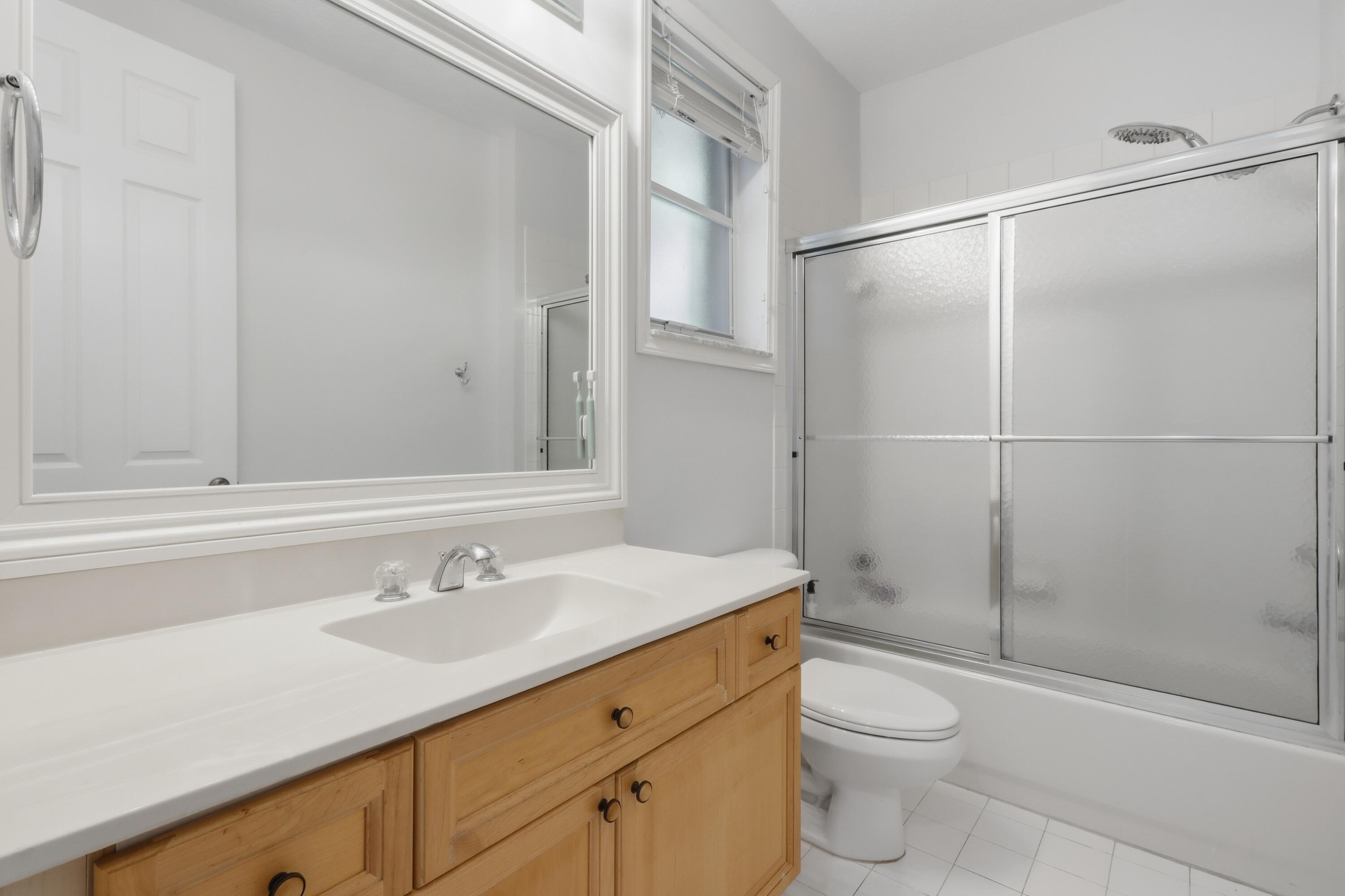 Bathroom featuring a wood-finish vanity with a rectangular sink, oversized wall-mounted mirror, white tile flooring, and a tub-shower combination with sliding glass doors