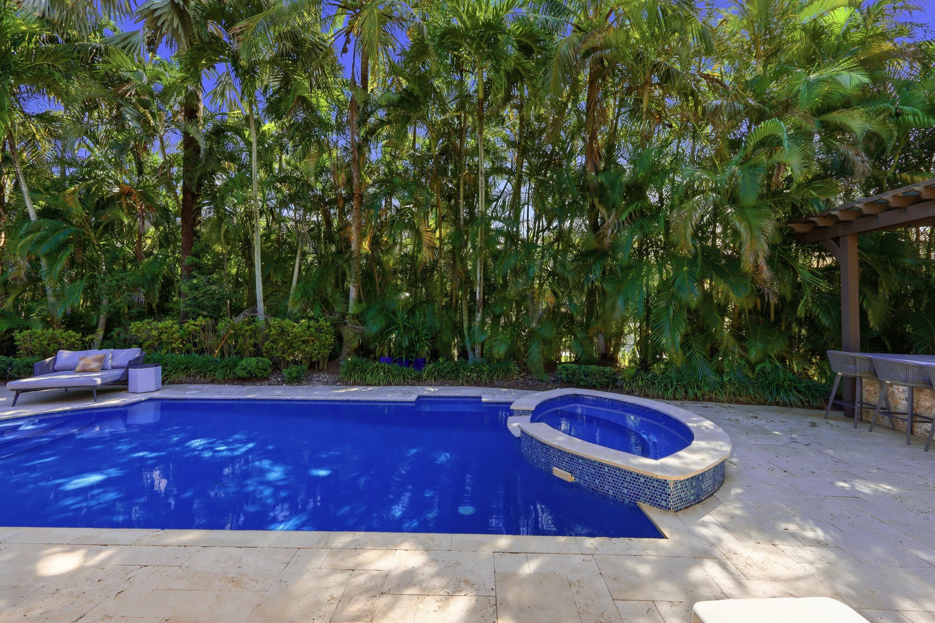 In-ground swimming pool with integrated elevated spa, stone pool decking, and wood-beam pergola