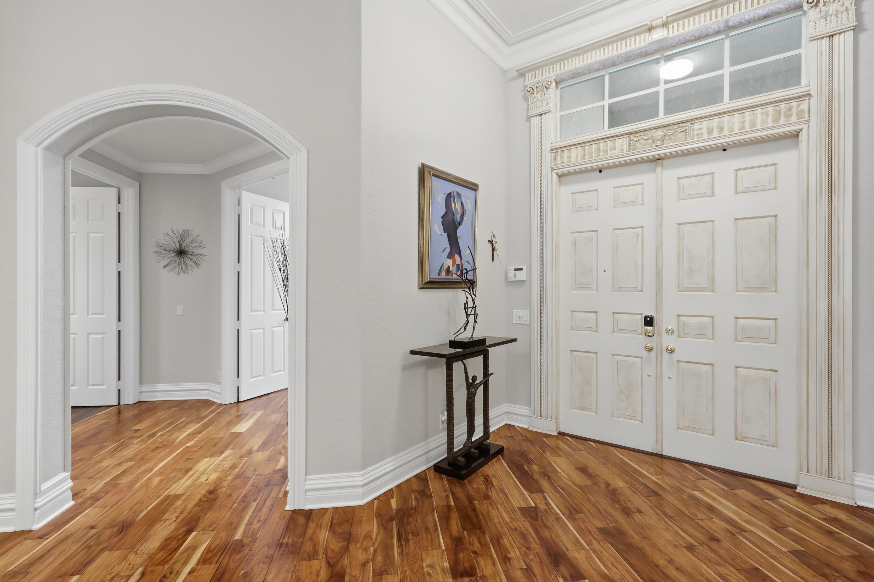 Entryway featuring dual paneled doors with decorative transom window, architectural crown molding, arched entryways, and wood-finish flooring Entryway featuring dual paneled doors with decorative transom window, architectural crown molding, arched entryways, and wood-finish flooring