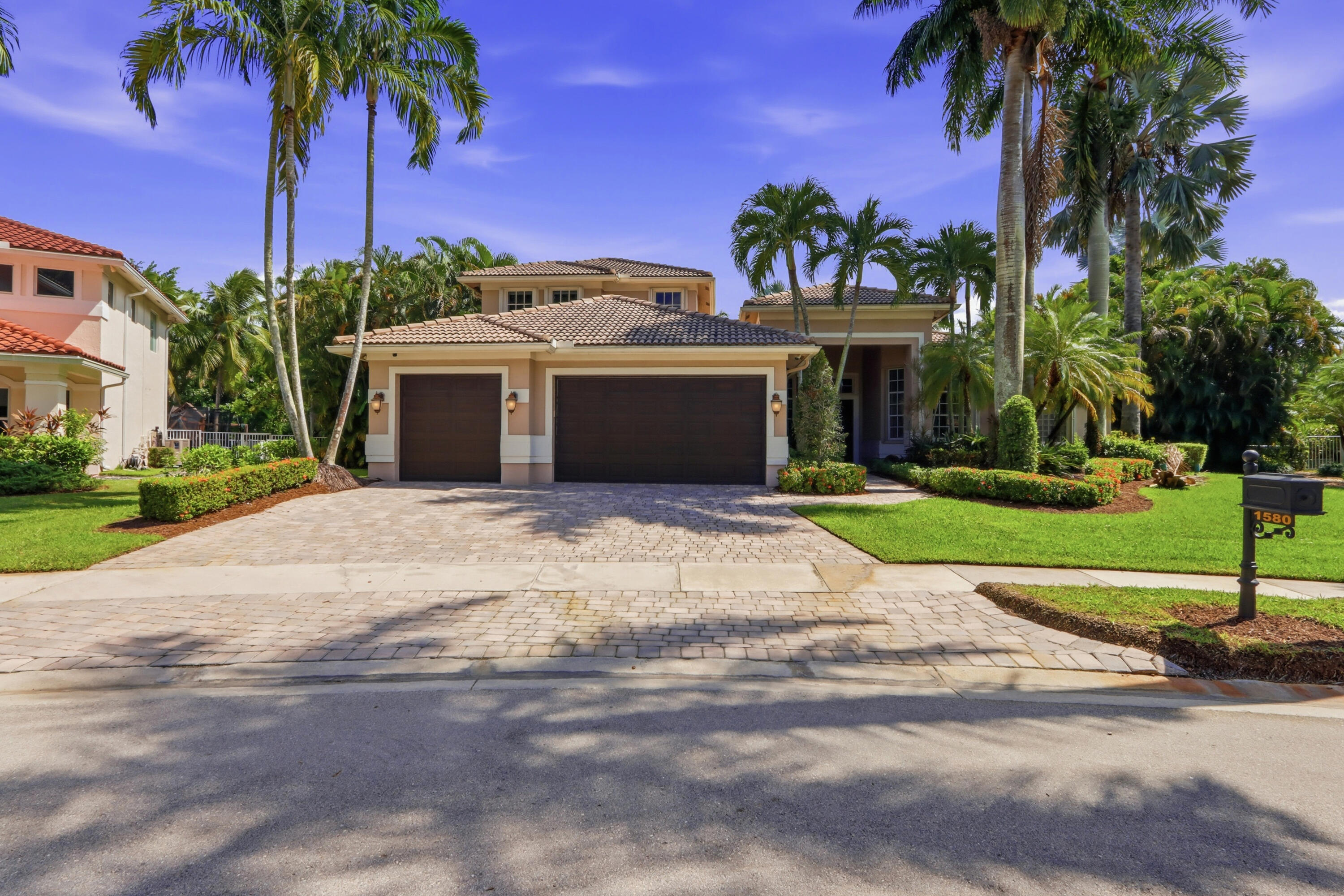 Multi-hipped tile roof, a three-car garage, and a paved stone driveway surrounded by manicured landscaping and mature palm trees Multi-hipped tile roof, a three-car garage, and a paved stone driveway surrounded by manicured landscaping and mature palm trees