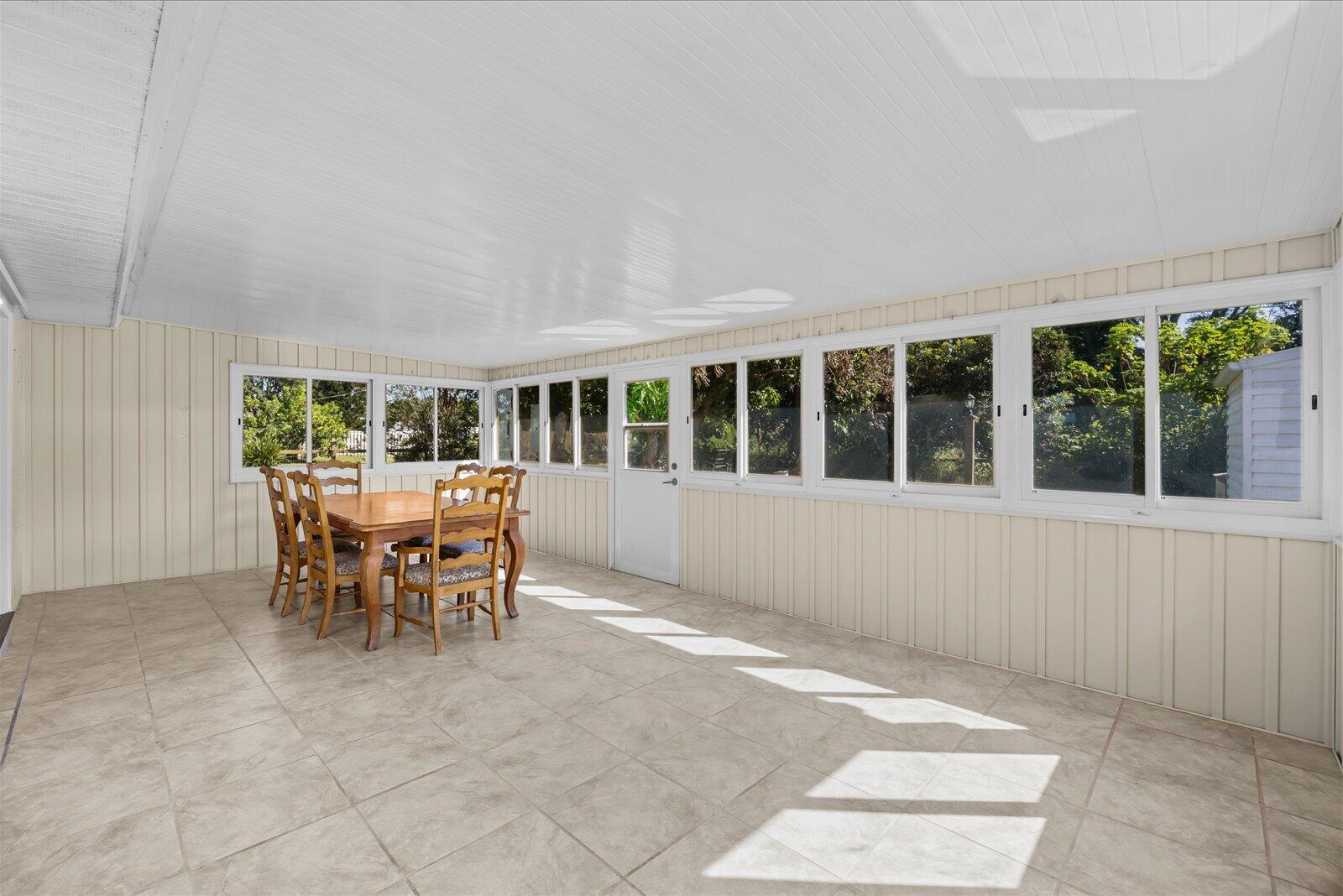 Enclosed sunroom featuring large paneled windows, neutral tile flooring, light-toned vertical paneling, and a painted beadboard ceiling