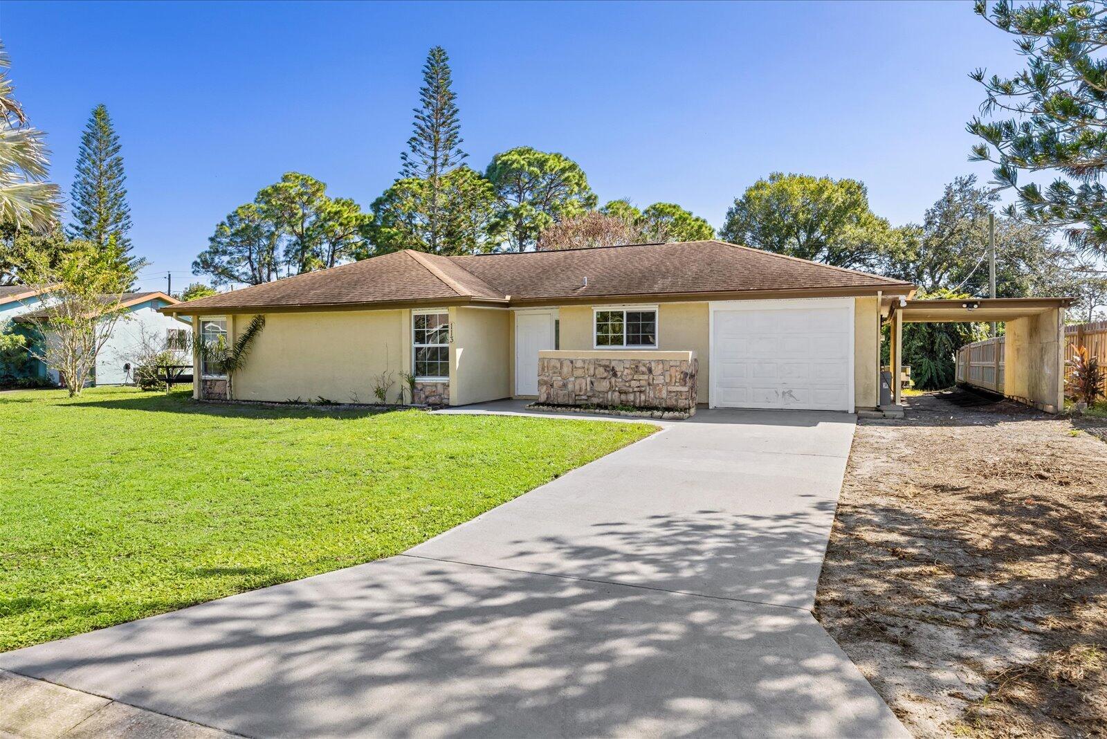 Single-story exterior featuring a stone-veneer accent wall, a concrete driveway, an attached garage, and a covered side carport