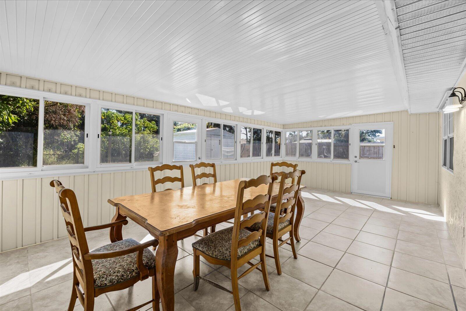 Enclosed sunroom featuring light-toned tile flooring, beadboard-style ceiling, extensive glass window pane wall, and a solid-panel exterior door with glass insert