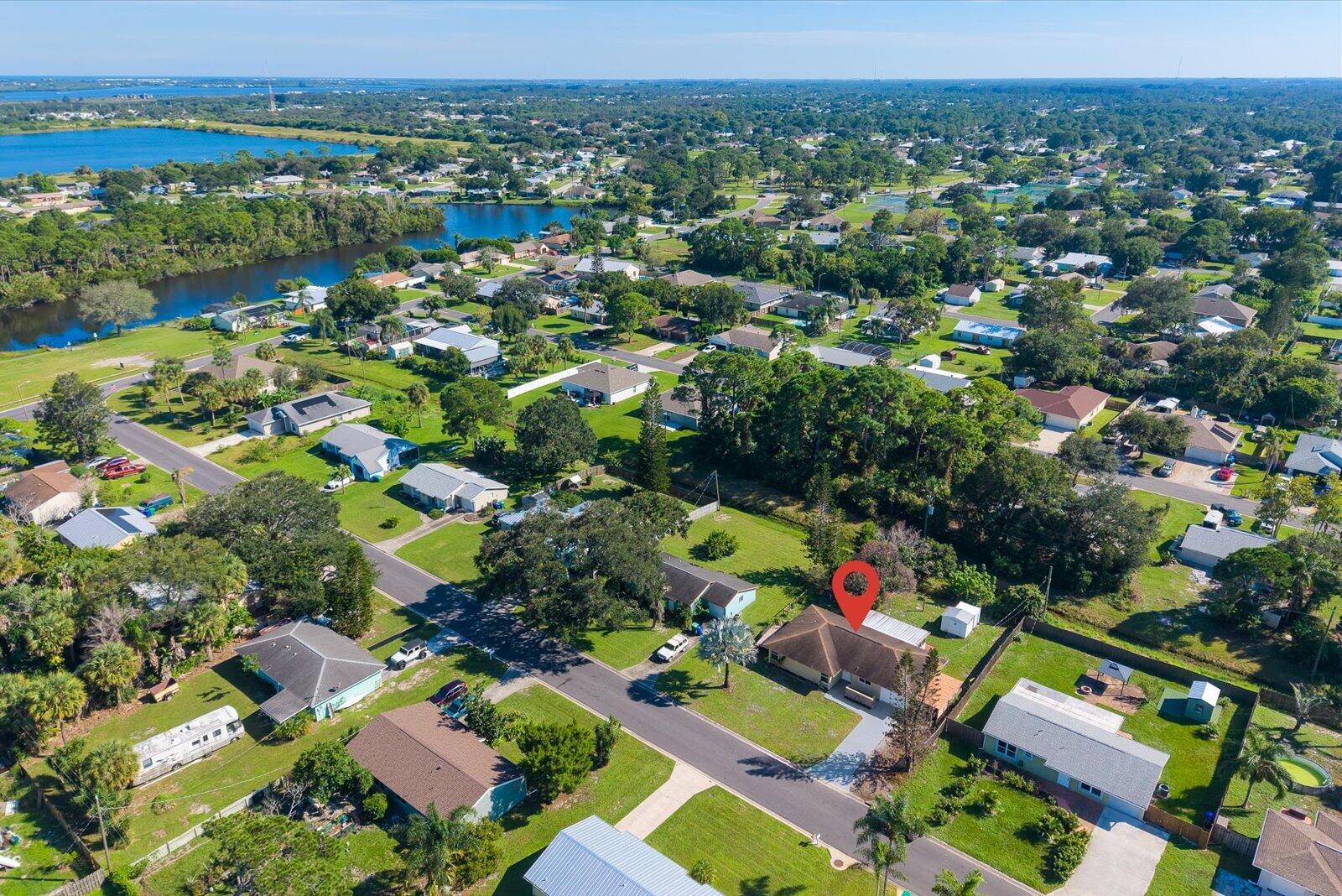 Aerial perspective of a residential property featuring a pitched roofline, paved driveway, expansive lawn, and mature canopy trees