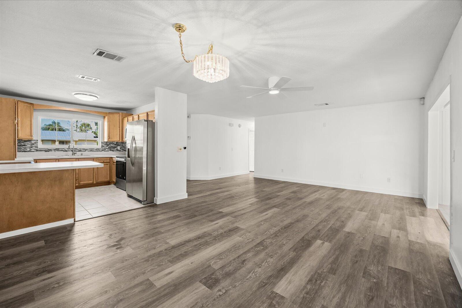 Open-concept interior featuring wood-finish flooring, a kitchen with light-tone cabinetry, stainless steel appliances, a crystal-style chandelier, and a white ceiling fan