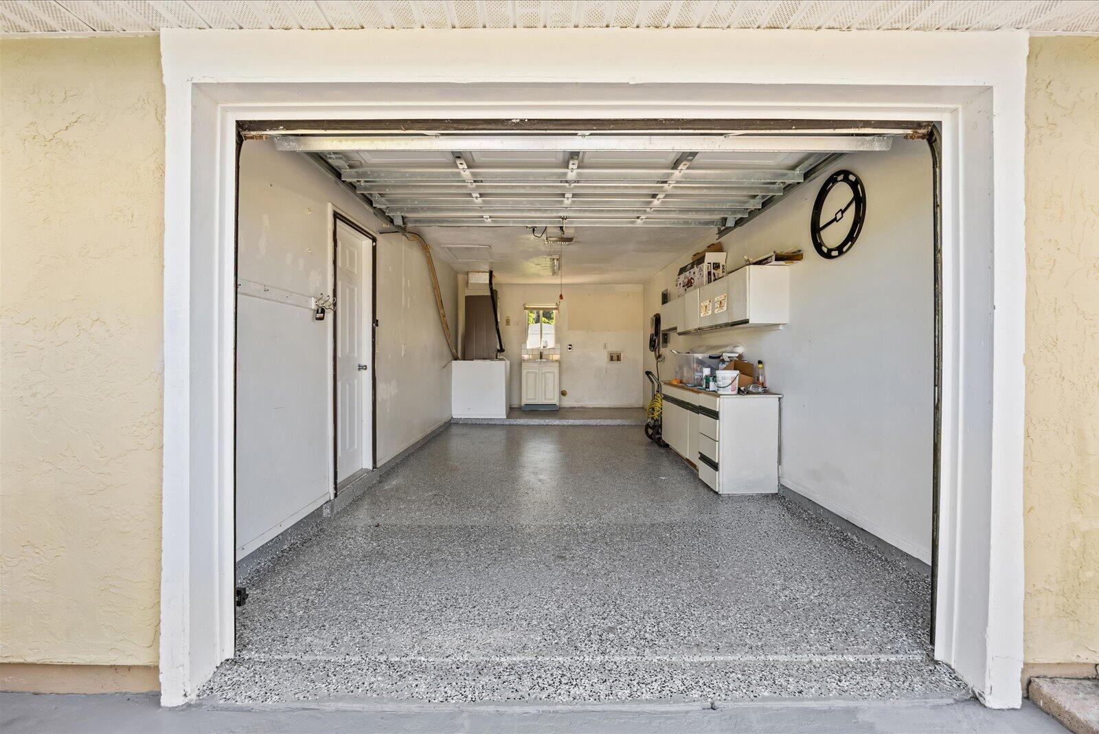 Enclosed garage featuring durable epoxy-coated flooring, built-in wall cabinetry, and a utility sink