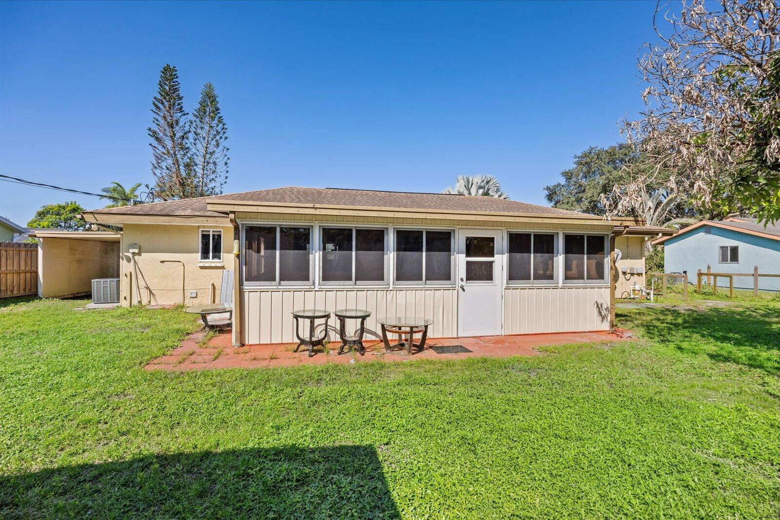 Enclosed rear porch featuring screen panels and a solid entry door, situated on a grass-covered lot with a paved patio