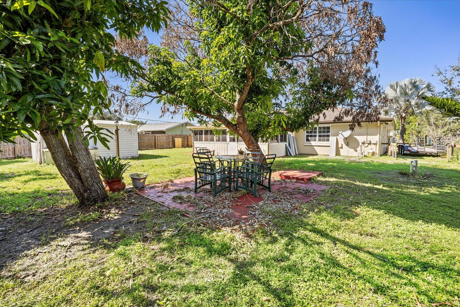Spacious backyard featuring a dedicated paved patio area, mature shade trees, and a detached storage structure enclosed by wood perimeter fencing