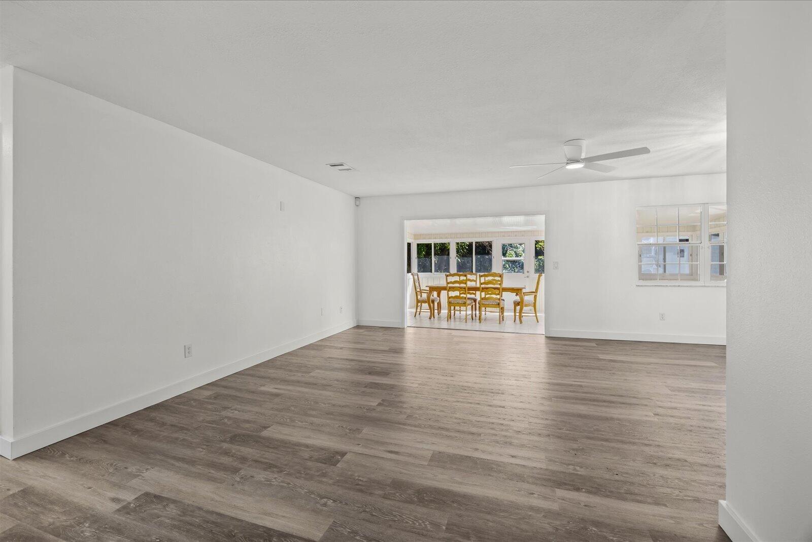 Open floor plan featuring wood-finish flooring, neutral wall tones, multi-pane windows, and a ceiling fan with integrated lighting