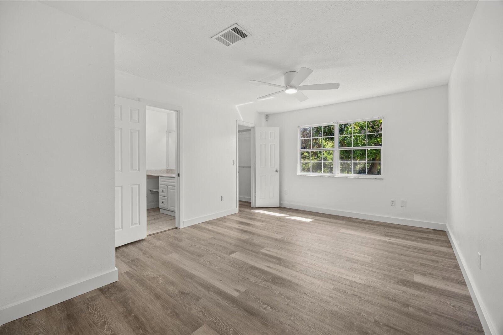 Neutral interior featuring wood-finish flooring, a multi-pane window, and a ceiling-mounted light fixture with fan blades