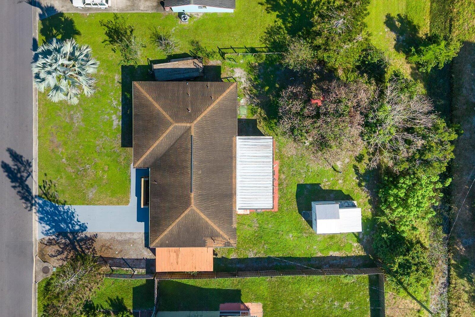 Aerial perspective of property featuring a hip-style roof, a paved driveway, a metal-covered patio, a detached storage structure, and expansive grass landscaping