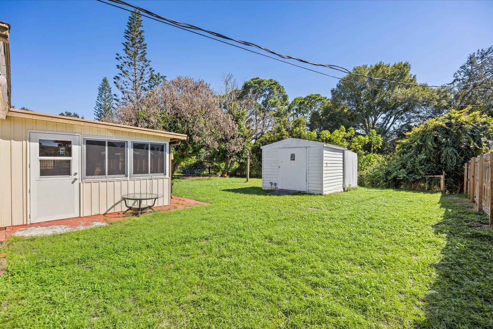 Expansive backyard featuring a level lawn, mature trees, a detached storage shed, and vertical panel siding exterior