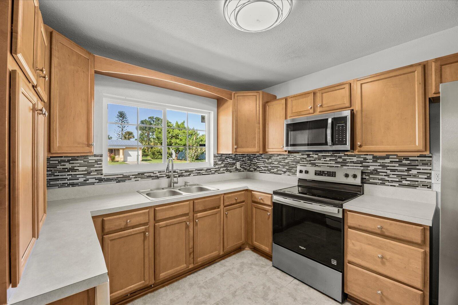 Kitchen featuring natural wood cabinetry, stainless steel appliances, a multi-tone tile backsplash, and solid surface countertops with a dual-basin sink