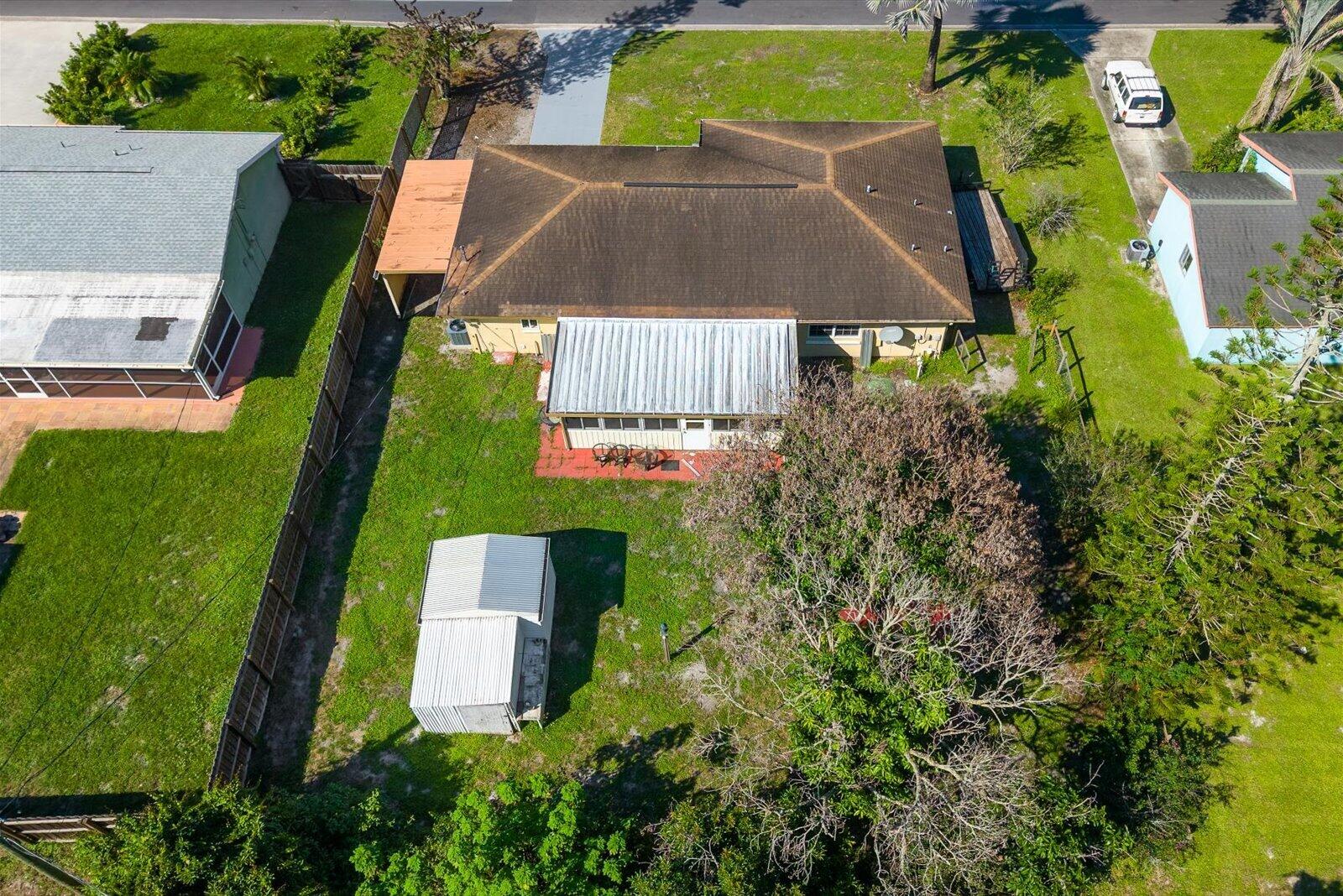 Aerial perspective of a detached property featuring a hip roof, a covered patio with a metal awning, an attached side carport, and a detached metal storage structure situated within a fenced rear lot