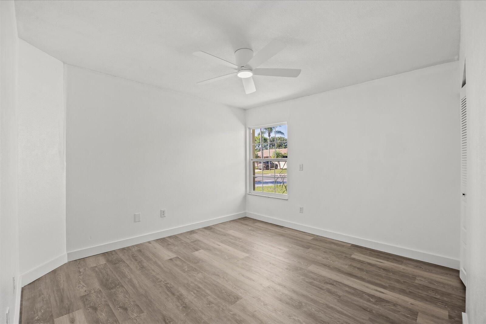 Interior room featuring wood-finish flooring, a neutral white color palette, a single-pane window, a ceiling-mounted light fixture, and a louvered closet door